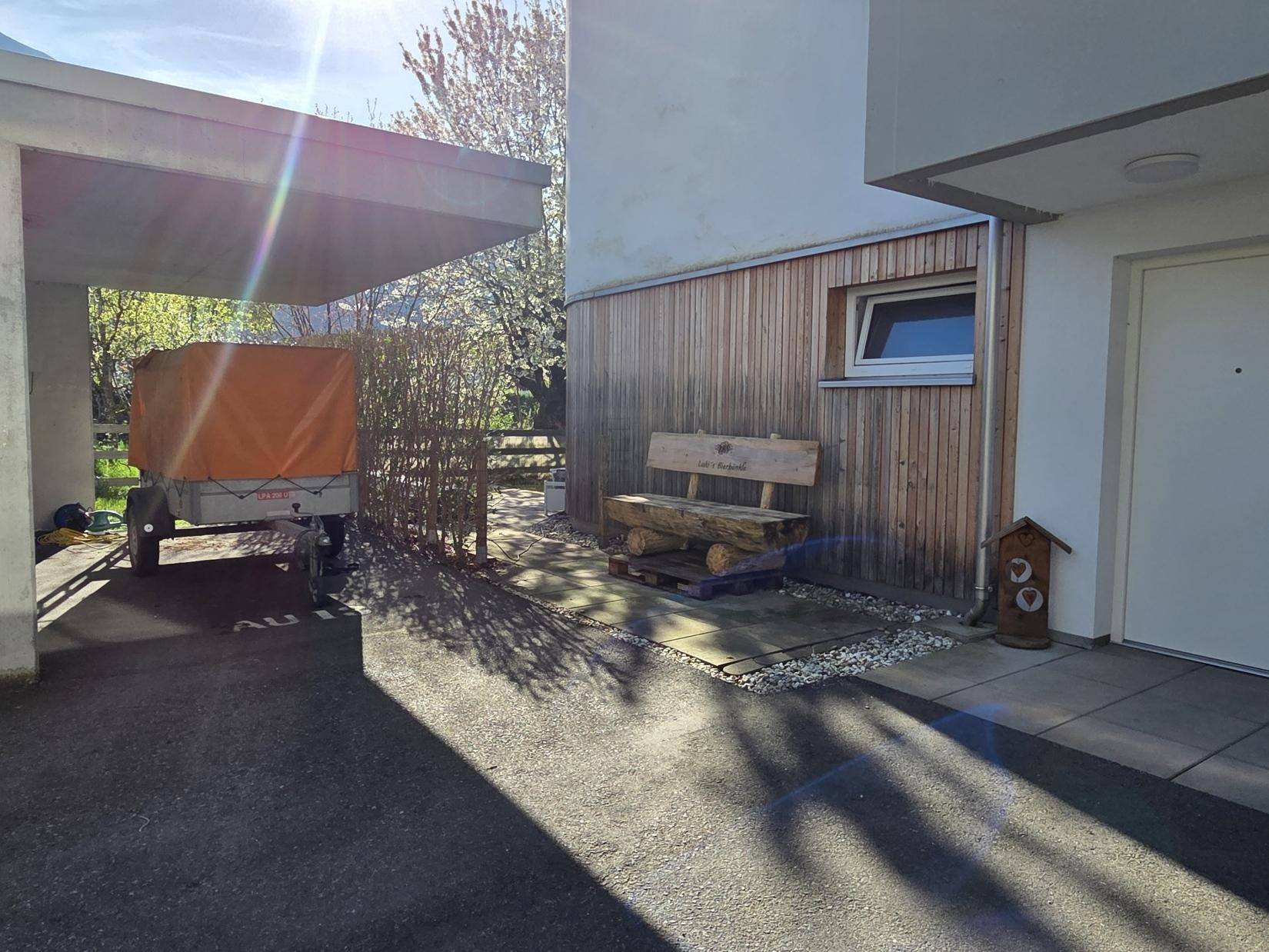Eingangsbereich mit Carport, einer rustikalen Holzbank und moderner Holzfassade.