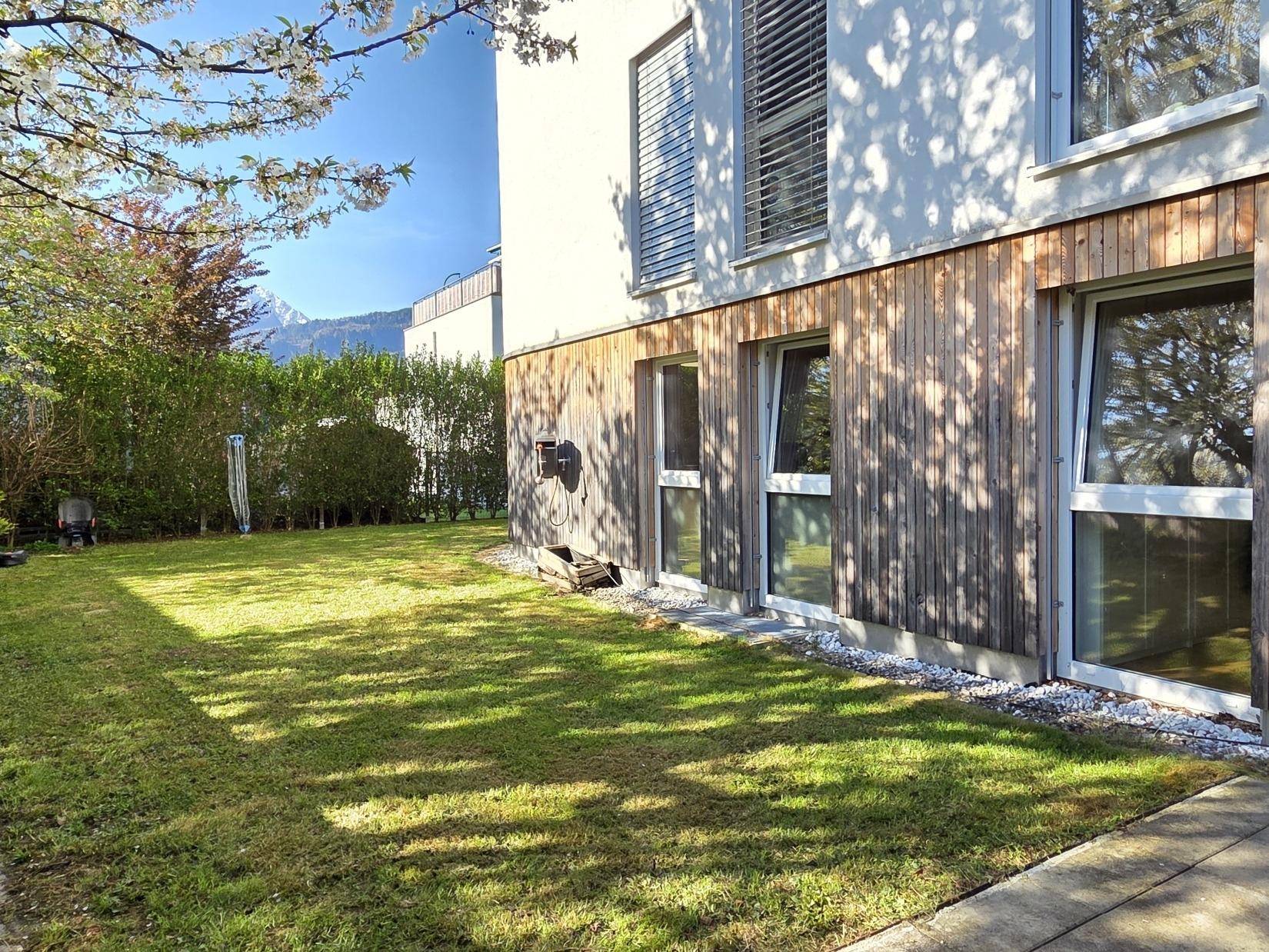 Gepflegter Gartenbereich neben dem Gebäude mit Rasen und Holzfassade, Bergblick.