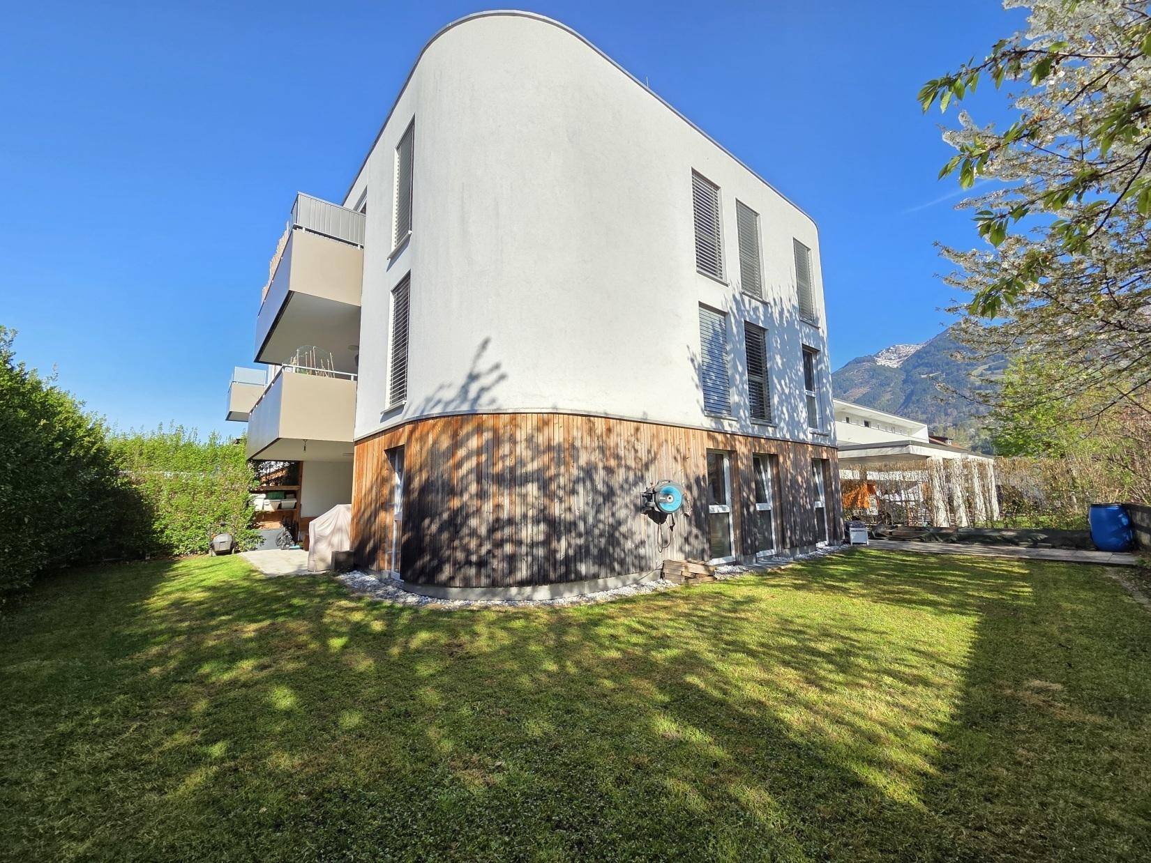 Moderne Architektur des Gebäudes mit geschwungener Fassade, Balkonen und gepflegtem Rasen.