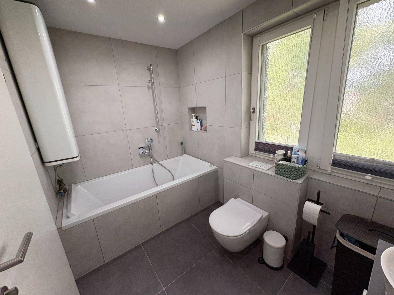 Helles Badezimmer mit Badewanne, WC und Fenster für natürliche Belüftung.