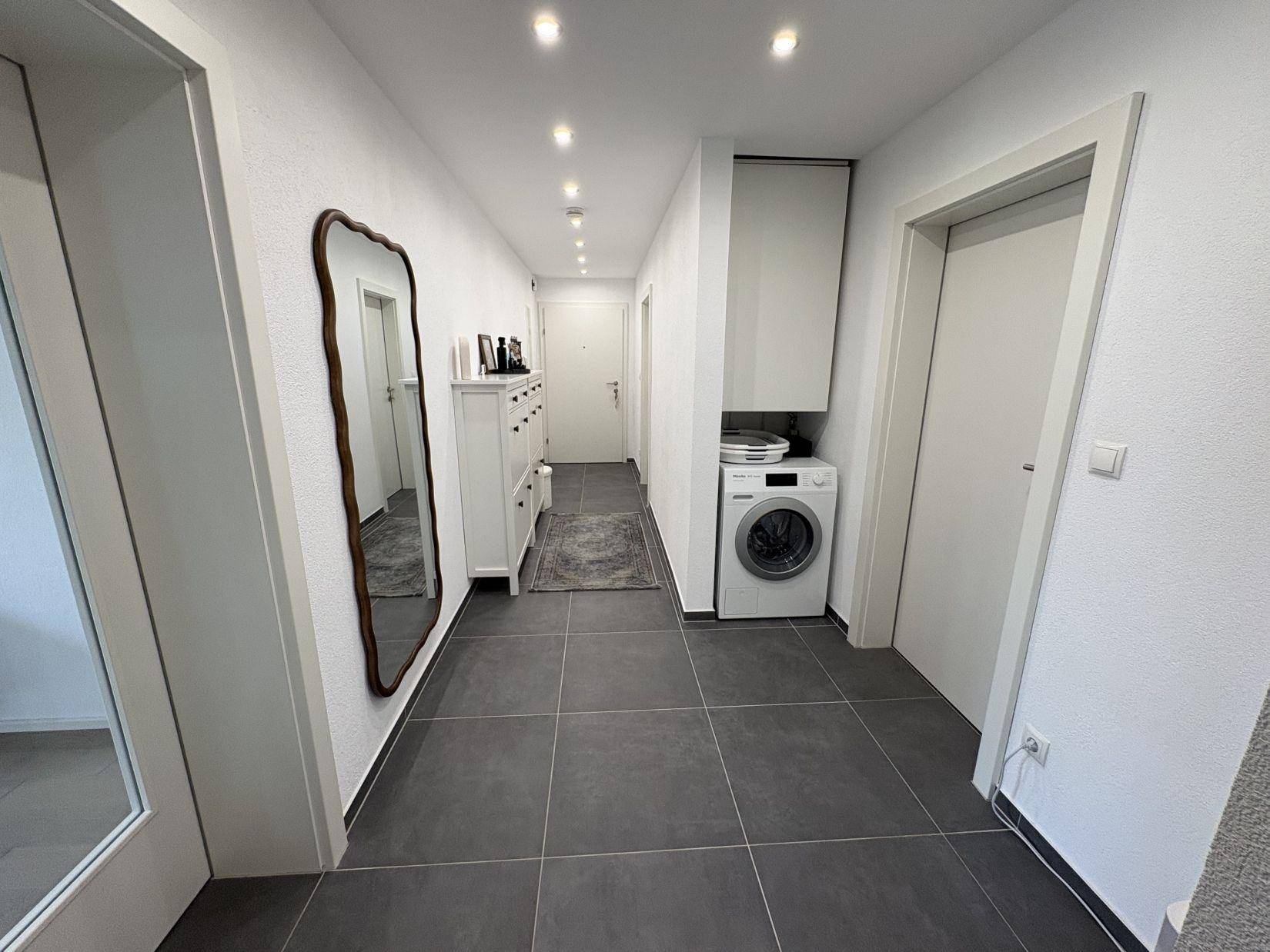 Langer Flur mit Fliesenboden, Waschmaschine und Einbauschrank.