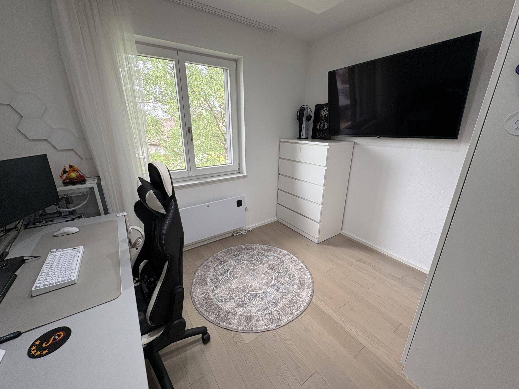 Modernes Arbeitszimmer mit Schreibtisch, Gaming-Setup und hellem Holzboden.