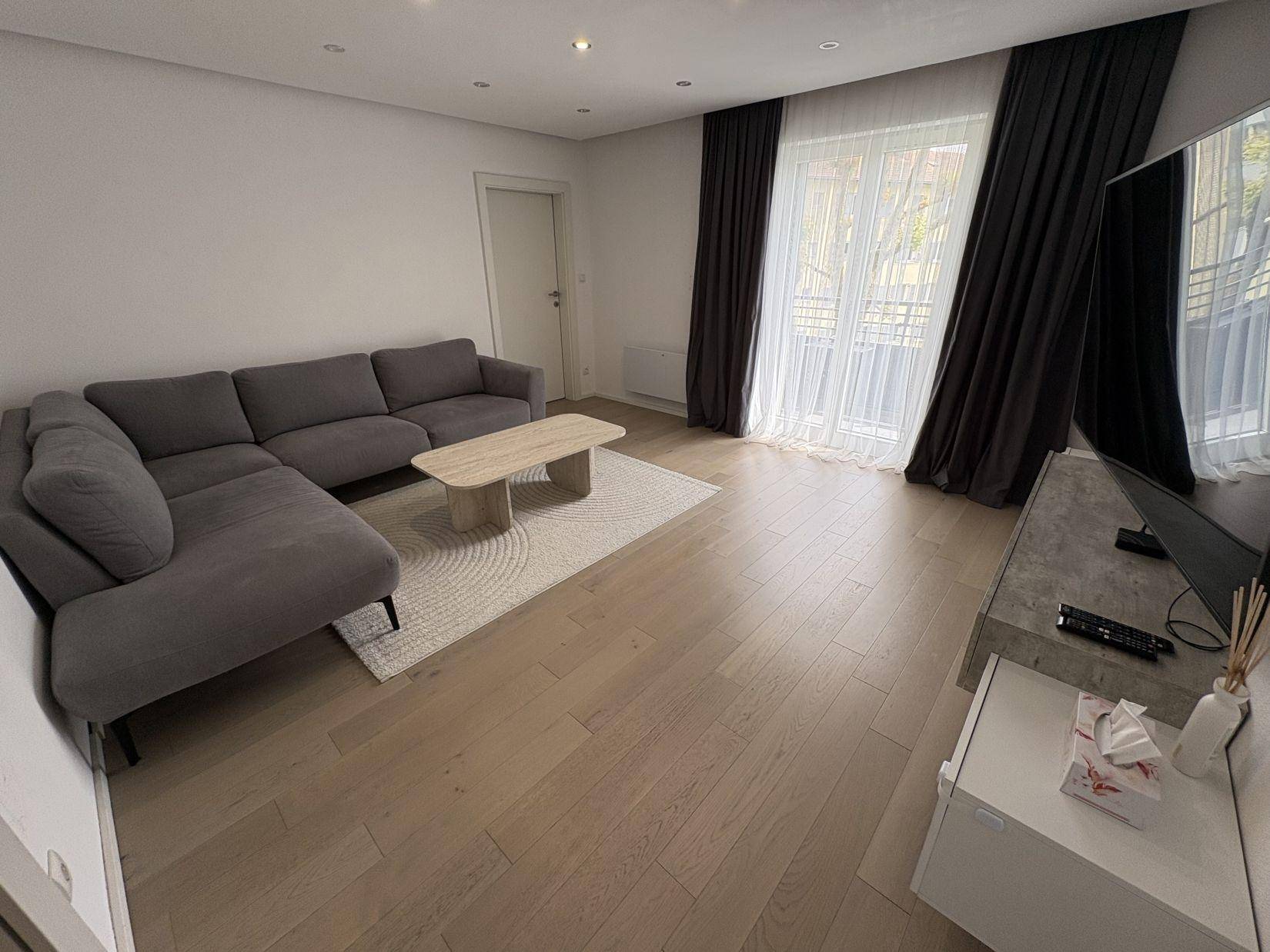 Modernes Wohnzimmer mit großem Ecksofa, hellem Holzboden und viel Tageslicht.
