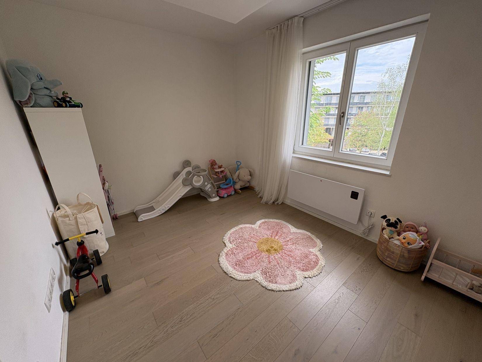 Freundliches Kinderzimmer mit Spielbereich, Holzboden und großem Fenster.