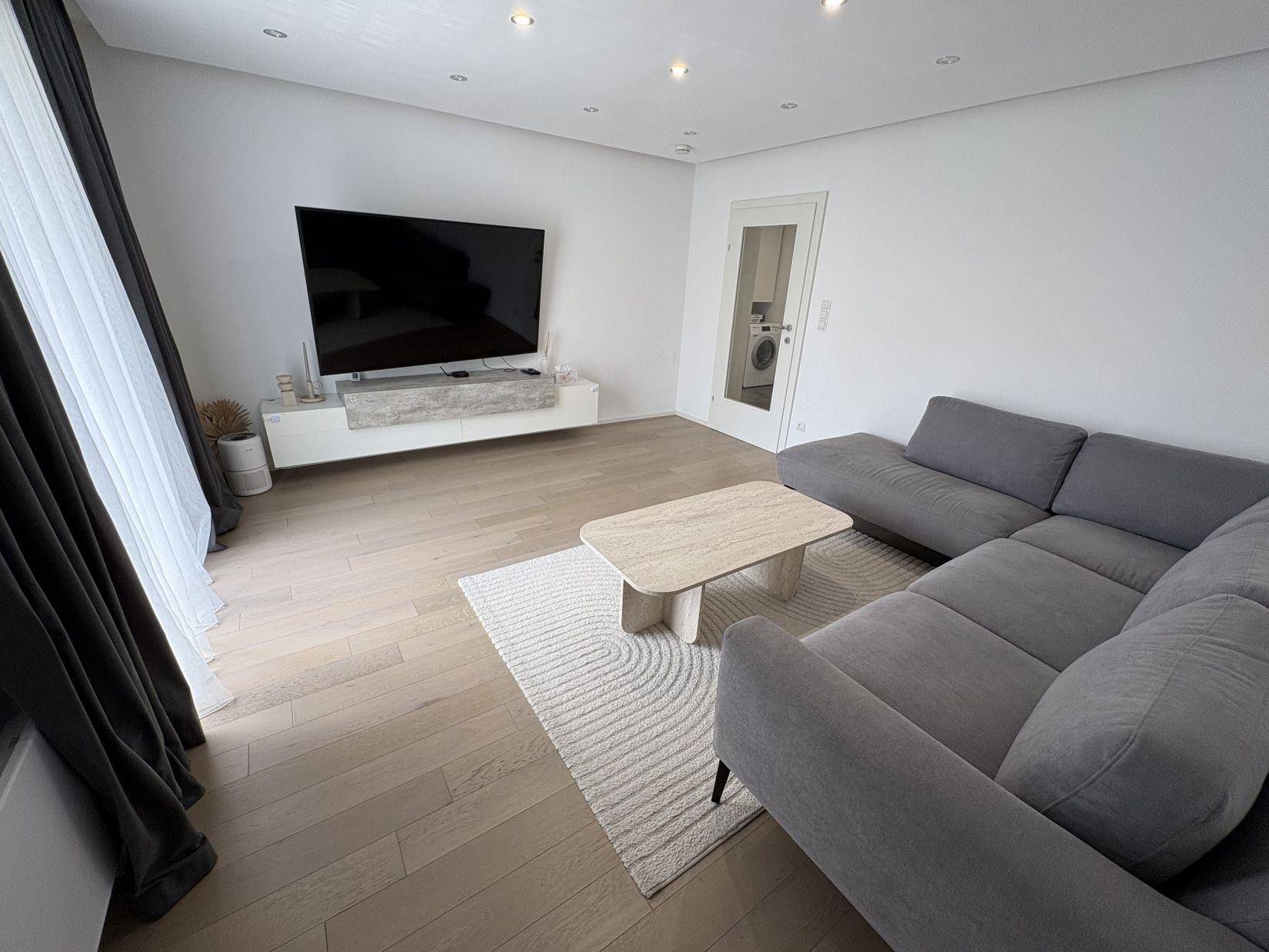 Helles Wohnzimmer mit großem Fernseher, modernem Couchtisch und Holzboden.