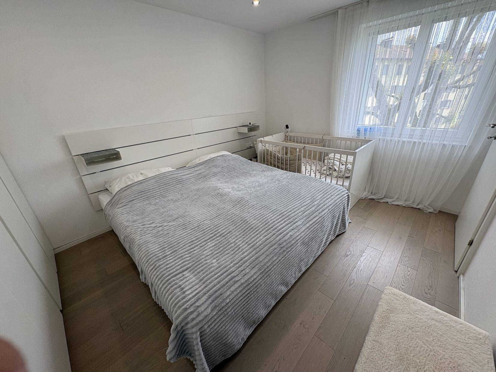 Gemütliches Schlafzimmer mit großem Fenster, Holzboden und viel Tageslicht.