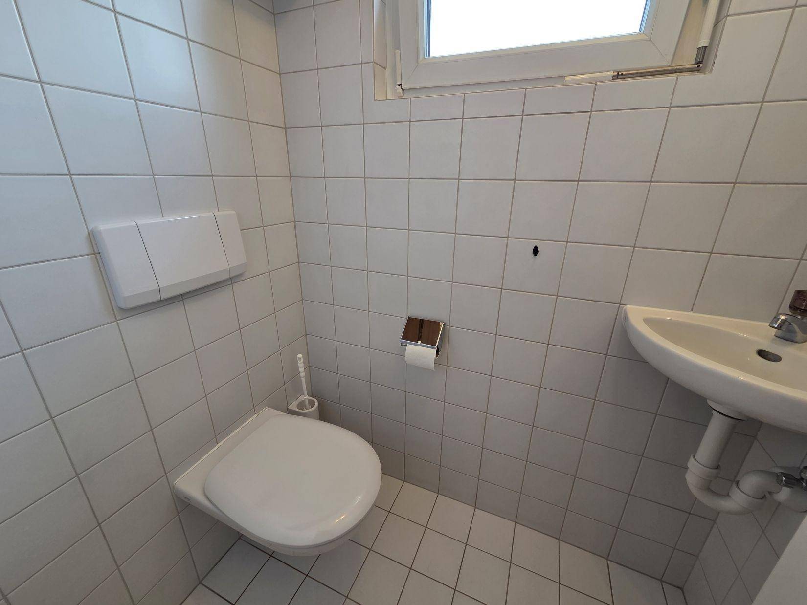 Kleines Gäste-WC mit Wand-WC, Waschbecken und einem Fenster für natürliche Belüftung.