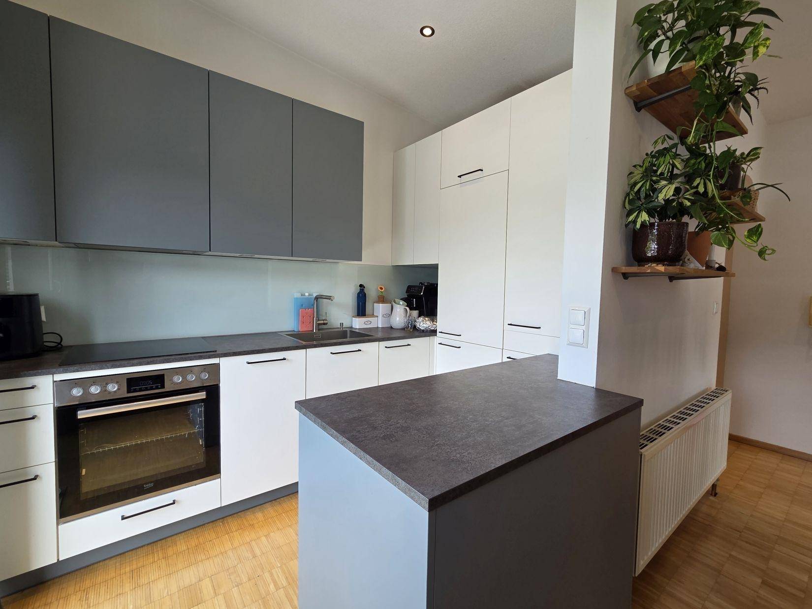 Moderne Küche mit grauen und weißen Schränken, integriertem Backofen und Holzparkettboden.