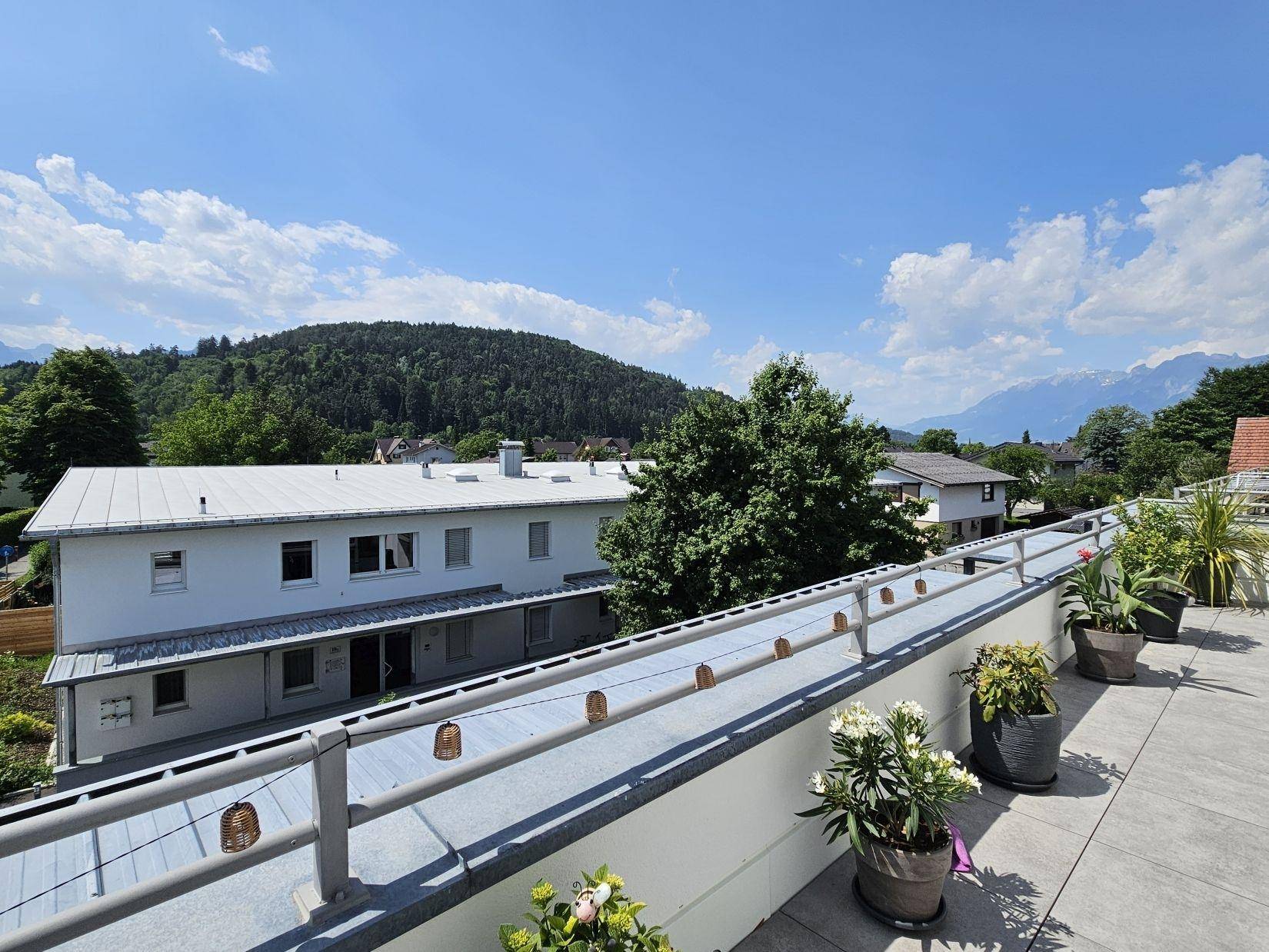 Sonnige Dachterrasse mit weitem Blick über die Dächer und die grüne Berglandschaft in der Ferne.