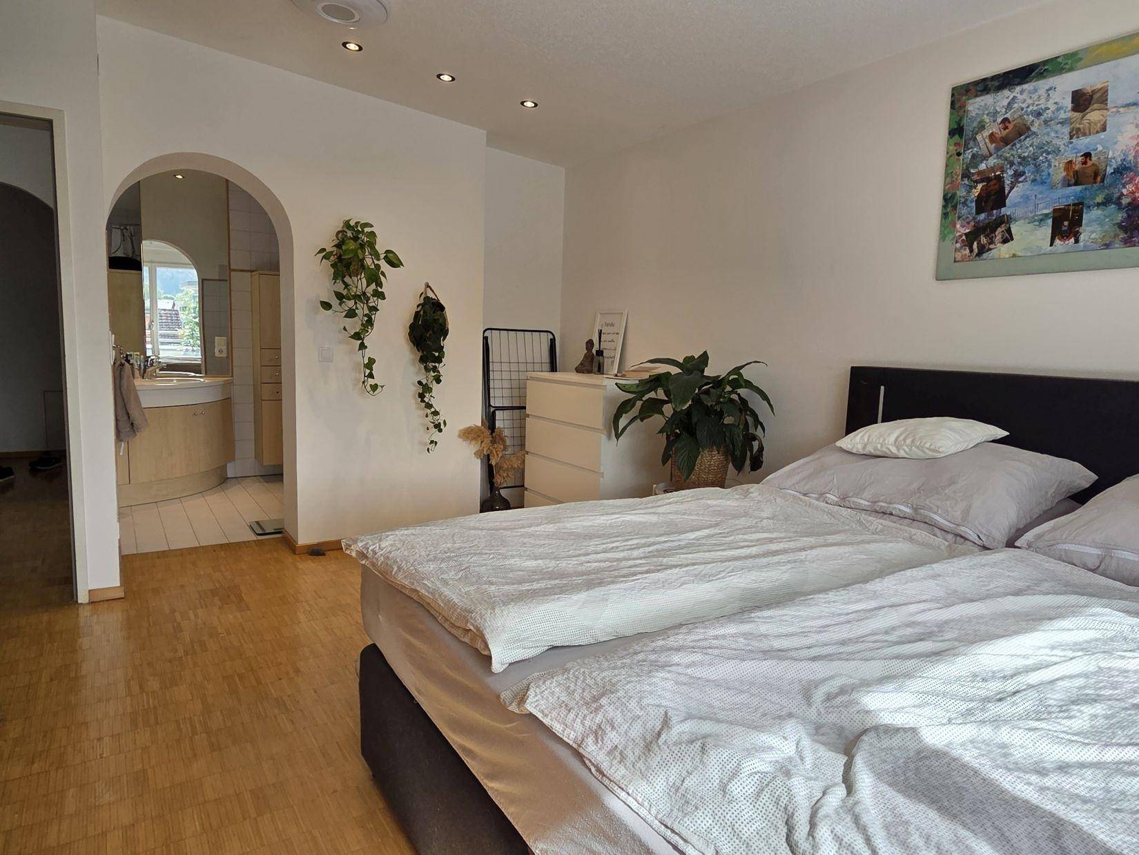 Geräumiges Schlafzimmer mit Doppelbett, Holzboden und offenem Zugang zum angrenzenden Badezimmer.