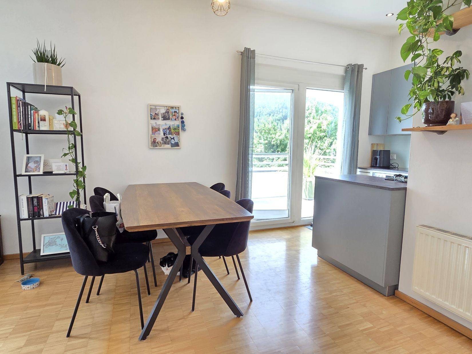 Essbereich mit modernem Holztisch, schwarzen Stühlen und Zugang zu einem sonnigen Außenbereich.