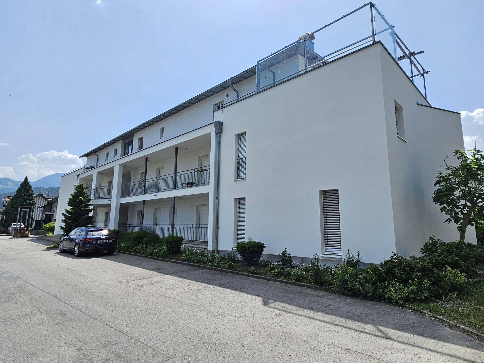 Ansicht eines modernen Wohngebäudes mit mehreren Balkonen und einer Dachterrasse unter blauem Himmel.