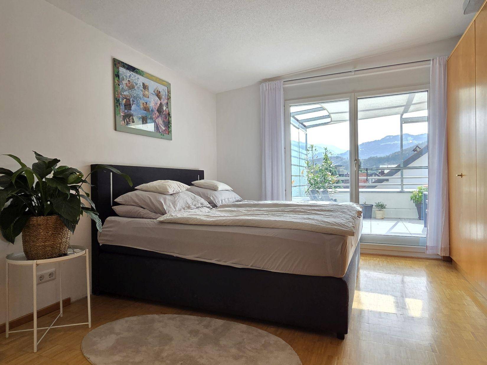 Helles Schlafzimmer mit Doppelbett, Holzparkett und direktem Zugang zur sonnigen Dachterrasse.