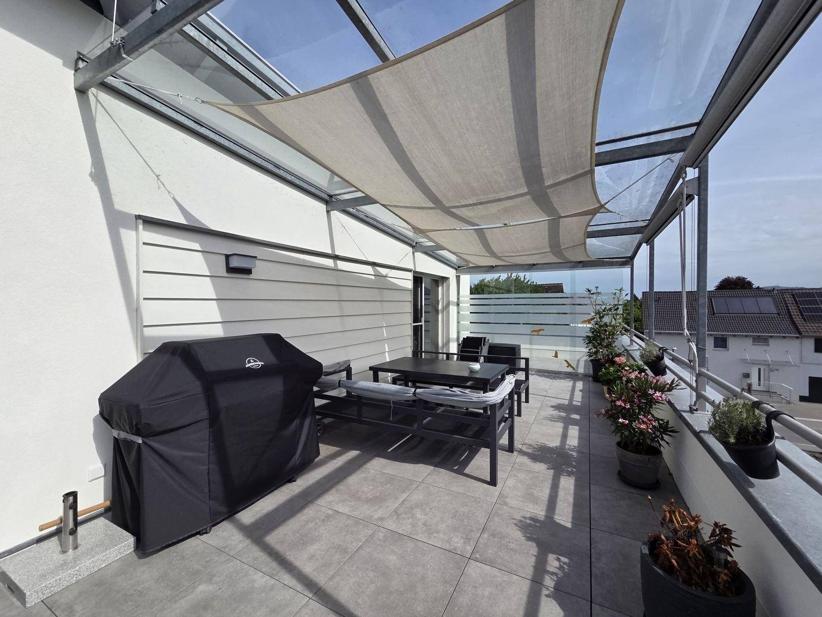Helle Dachterrasse mit Essbereich, Grill und Sonnenschutz, ideal für entspannte Stunden im Freien.