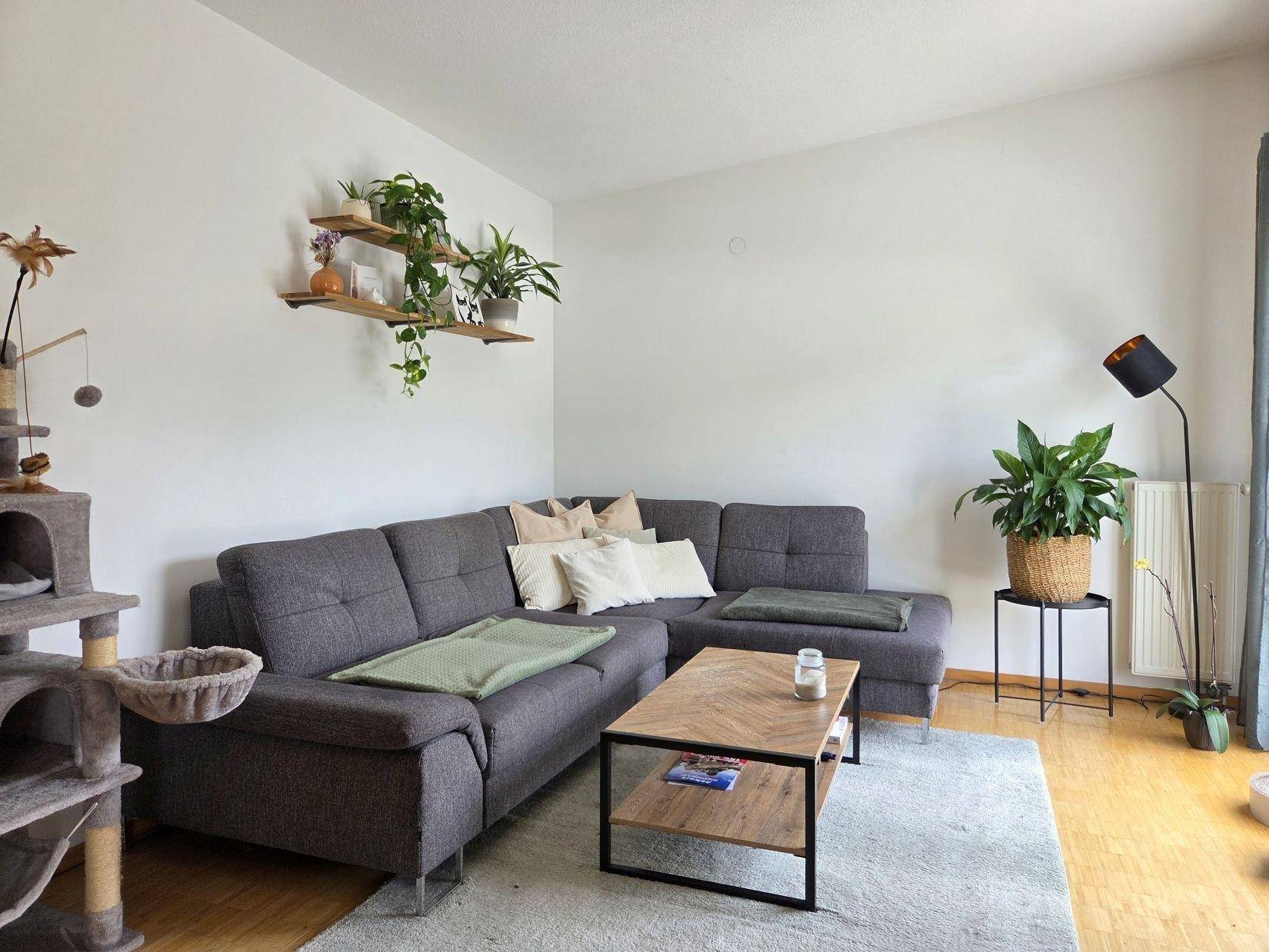 Gemütliches Wohnzimmer mit großem Ecksofa, Holzboden und vielen Pflanzen für eine wohnliche Atmosphäre.