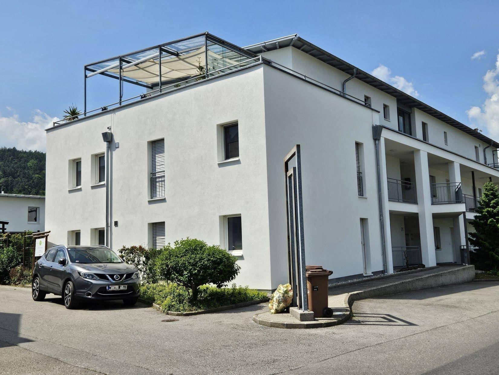 Modernes Mehrfamilienhaus mit weißer Fassade, Balkonen und einer Dachterrasse in sonniger Lage.