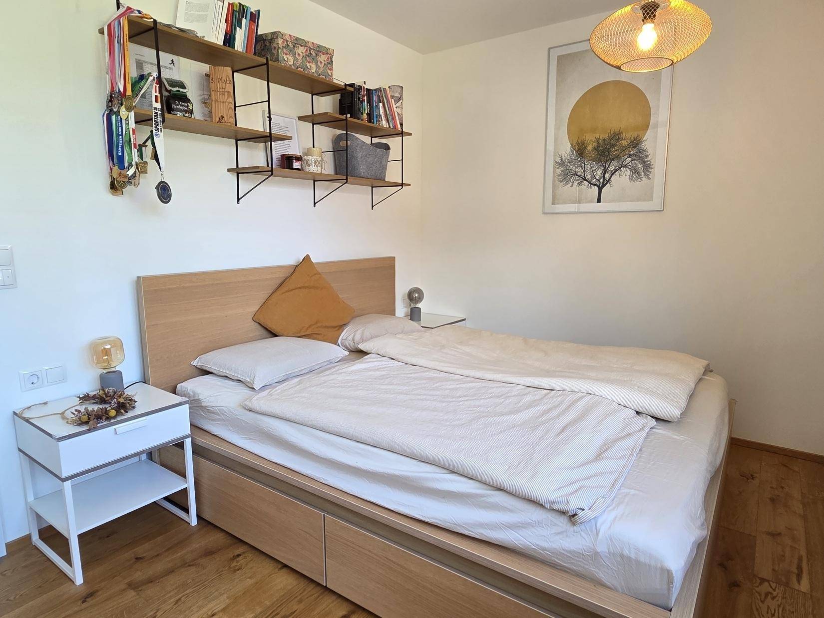 Helles Schlafzimmer mit Holzbett, Nachttisch und dekorativen Regalen an der Wand.