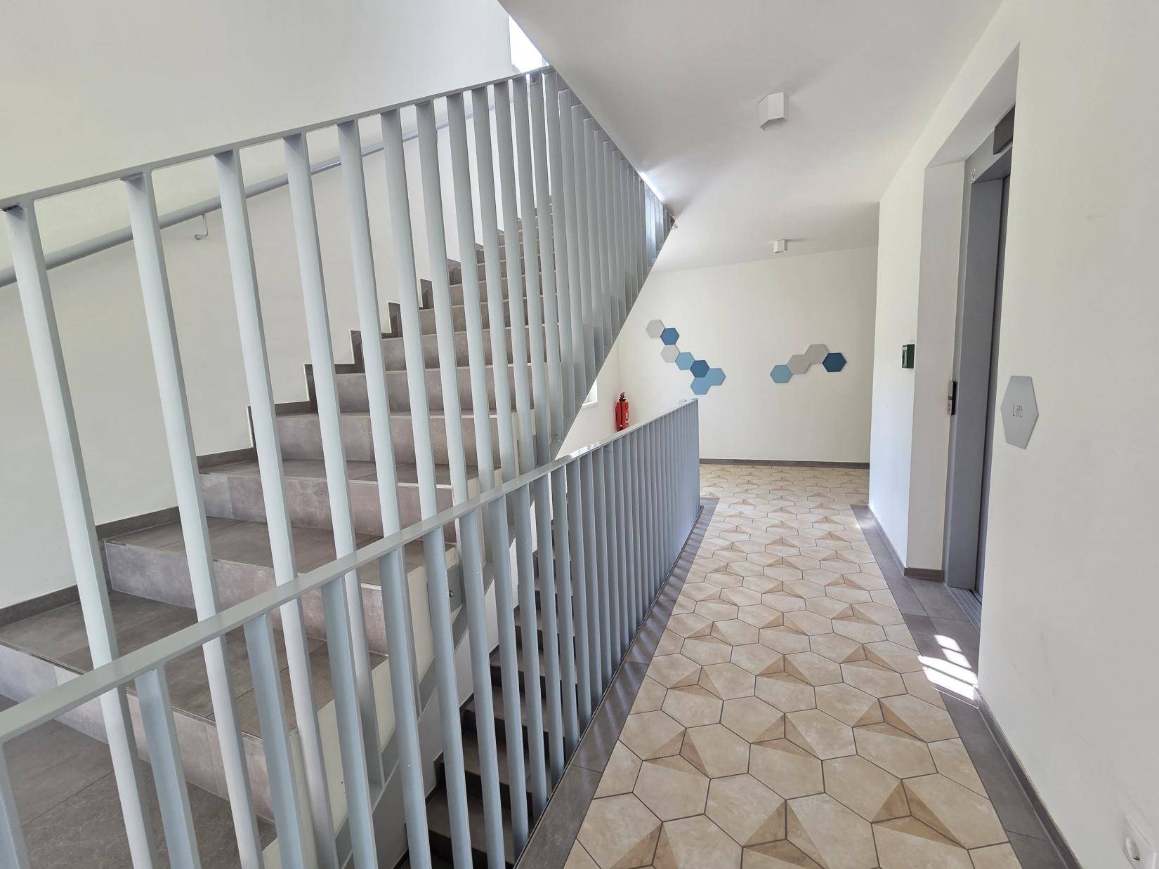 Modernes Treppenhaus mit hellem Geländer und dekorativen Bodenfliesen im Gemeinschaftsbereich.