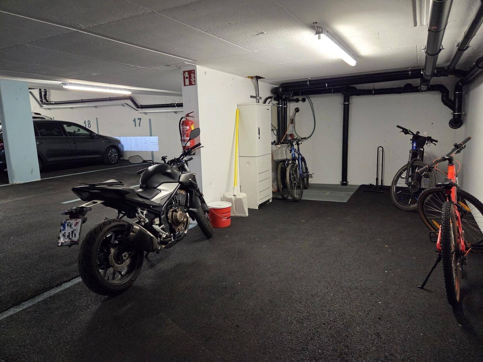 Tiefgarage mit Stellplätzen für Fahrzeuge und Fahrräder, inklusive sichtbarer Installationen an der Decke.