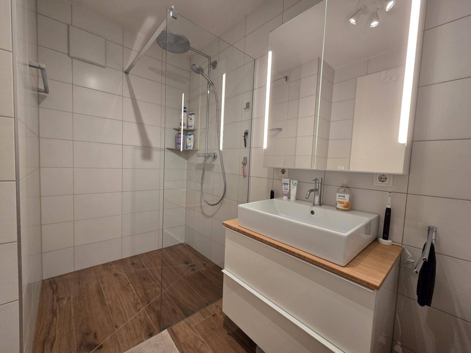 Modernes Badezimmer mit ebenerdiger Dusche, Einzelwaschbecken und beleuchtetem Spiegelschrank.