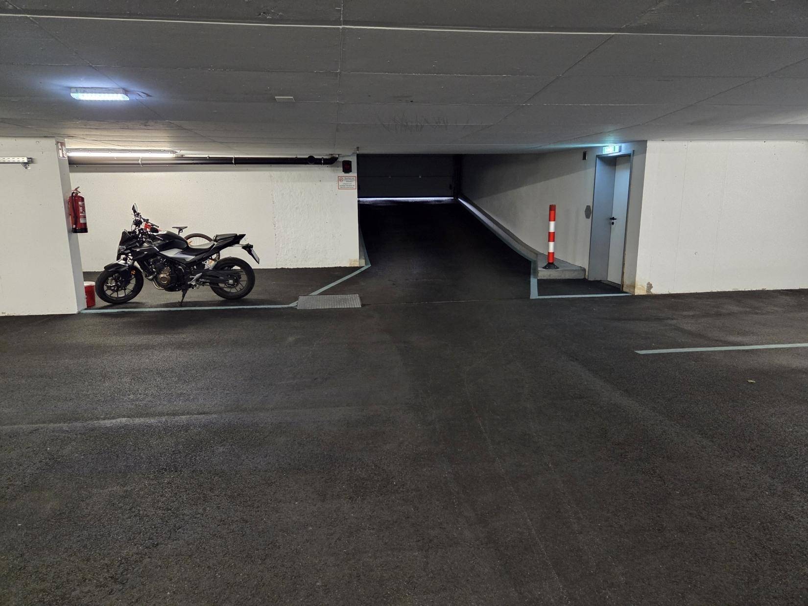 Einfahrt zur Tiefgarage mit geparktem Motorrad und gut beleuchtetem Zugang.
