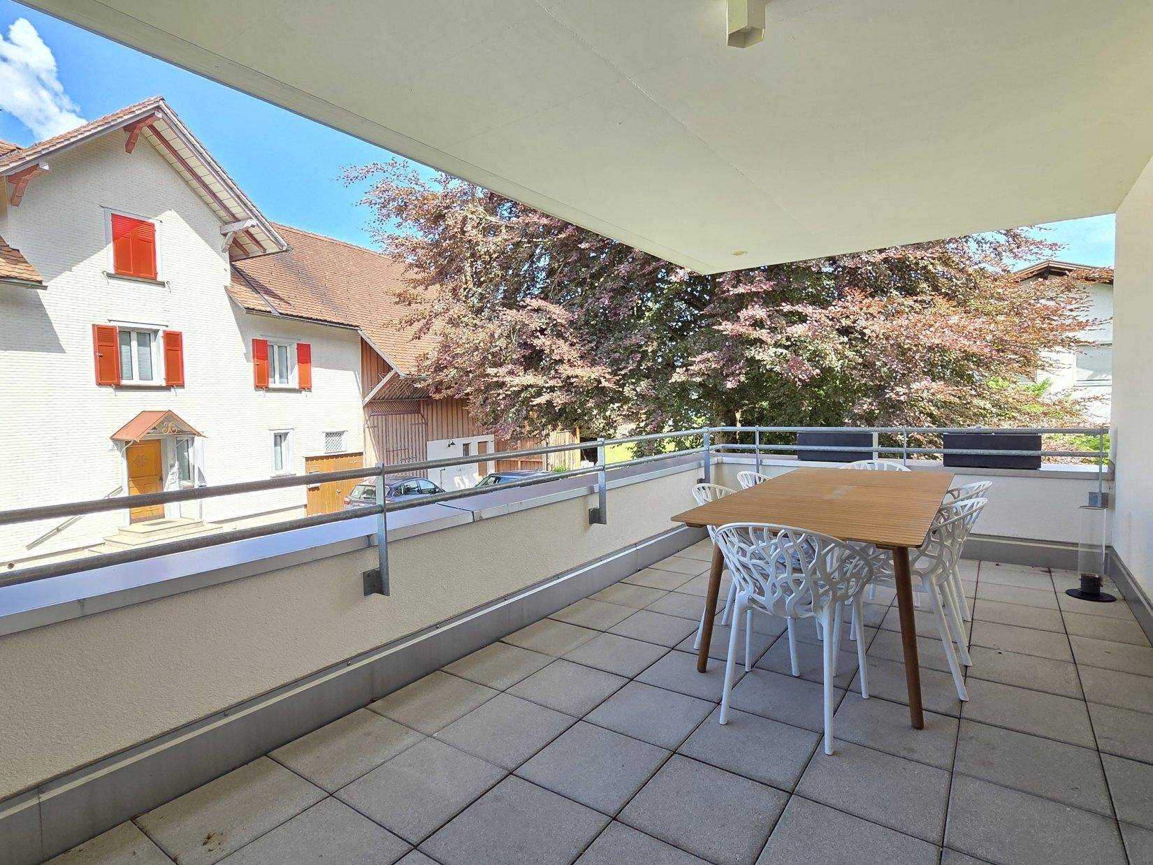 Überdachter Balkon mit Essbereich und Blick auf die Nachbarschaft und grüne Bäume.