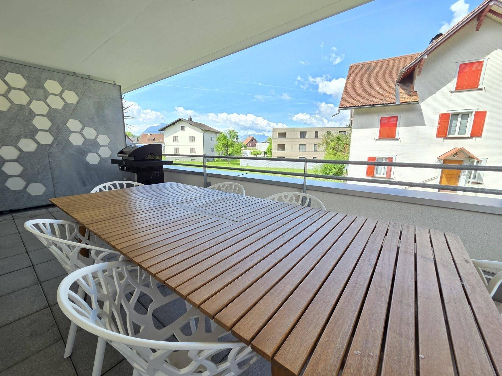 Sonniger Balkon mit Esstisch, Grill und weitem Blick über die Dächer und Berge.