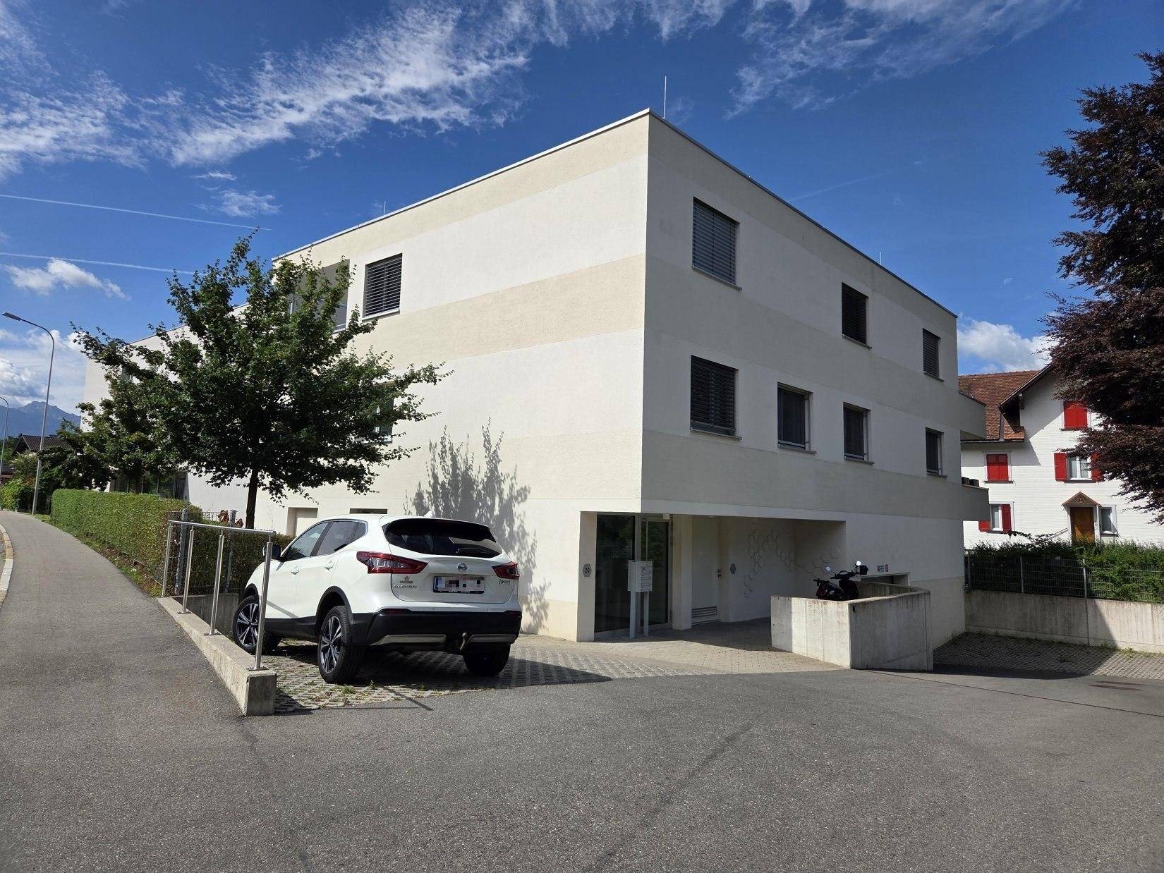 Modernes Mehrfamilienhaus mit schlichter Fassade und einem geparkten Auto an der Zufahrt.