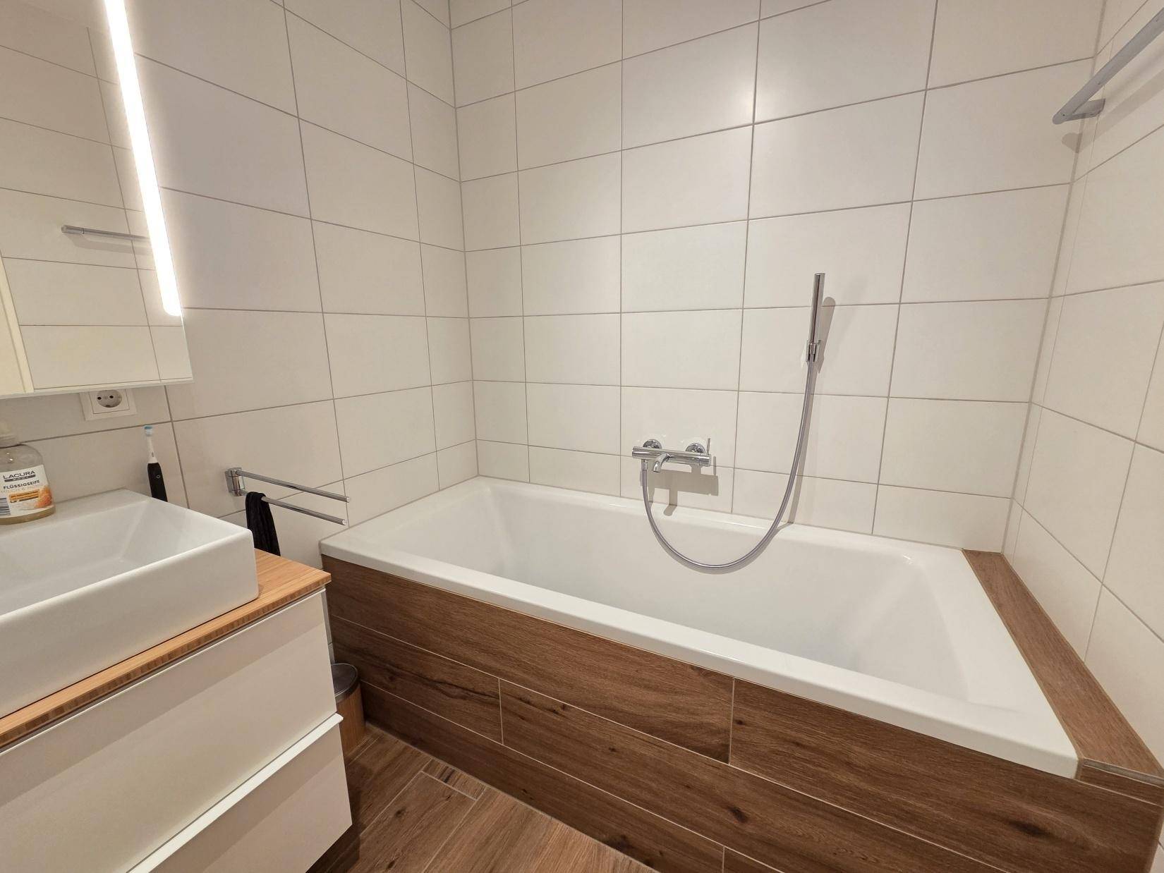 Helles Badezimmer mit Badewanne, Einzelwaschbecken und modernen weißen Fliesen.