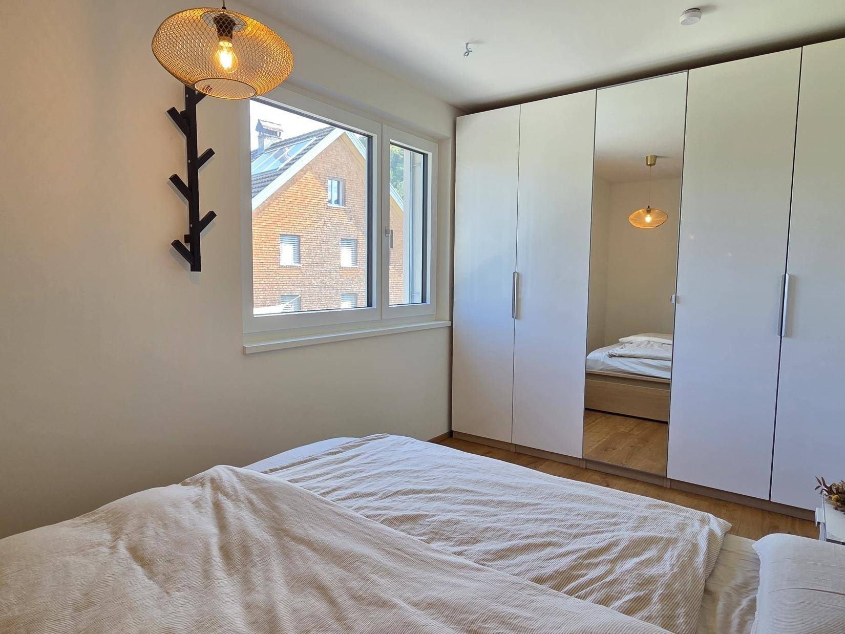 Schlafzimmer mit großem Spiegelschrank, Holzboden und Fenster mit Blick auf die Umgebung.