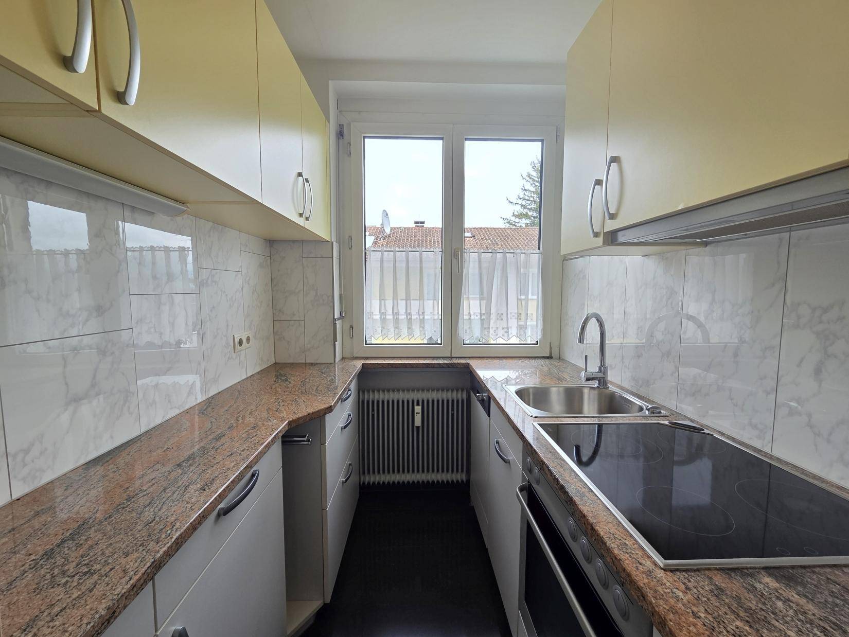 Funktionale Küche mit gelben Oberschränken, Granitarbeitsplatten und Fenster für Tageslicht.