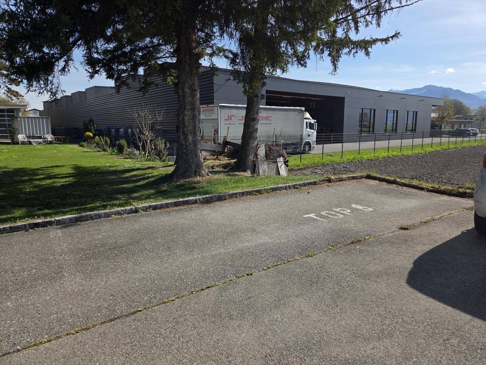 Außenansicht eines Gewerbegebäudes mit Parkplatz und LKW, umgeben von Grünflächen.