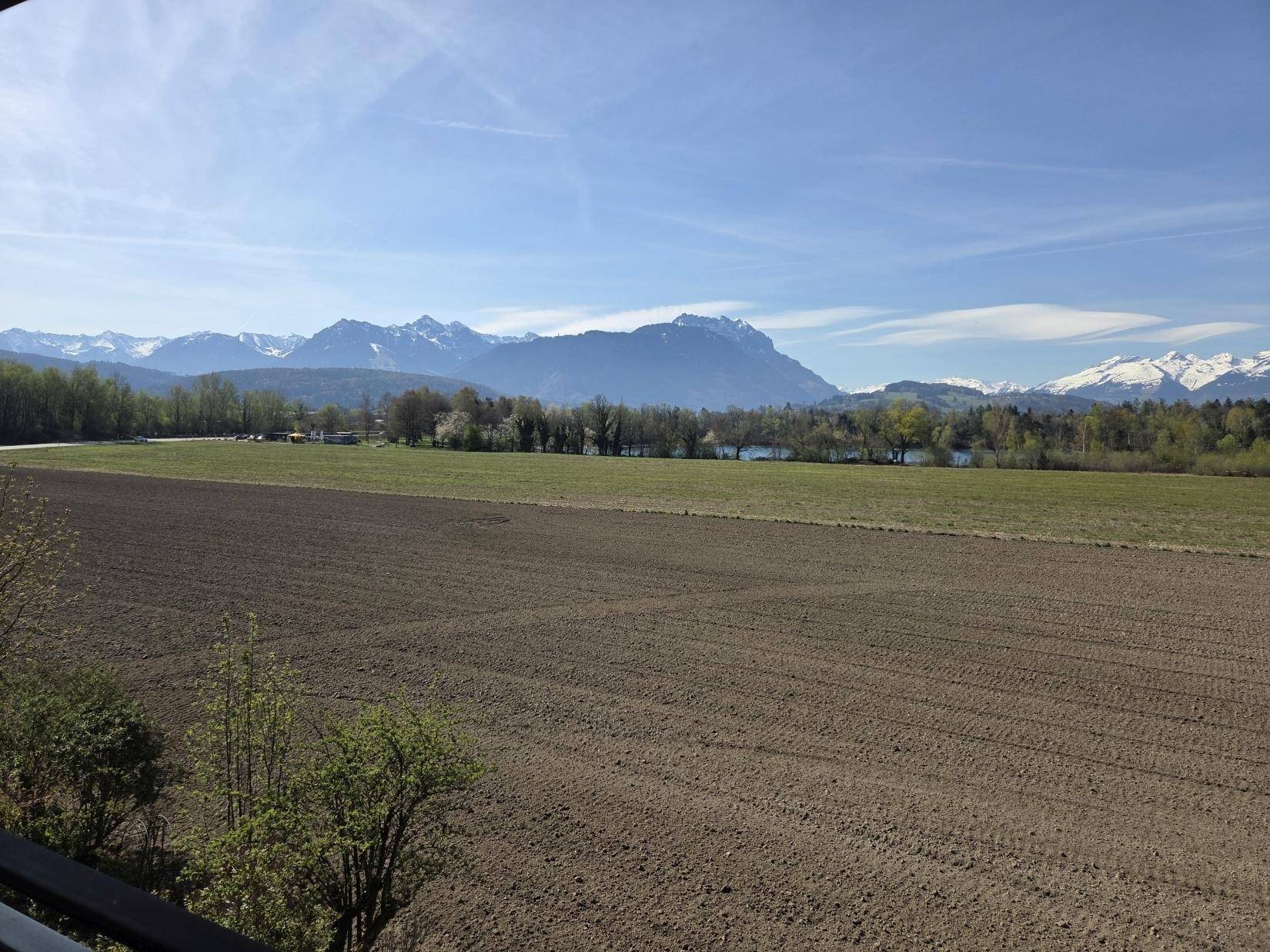 Weitläufiger Blick über Felder und einen See auf die majestätischen schneebedeckten Berge.