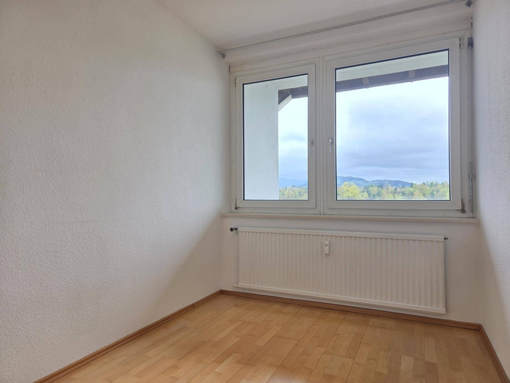 Helles Schlafzimmer mit Parkettboden und Fenster, das einen schönen Blick ins Grüne bietet.