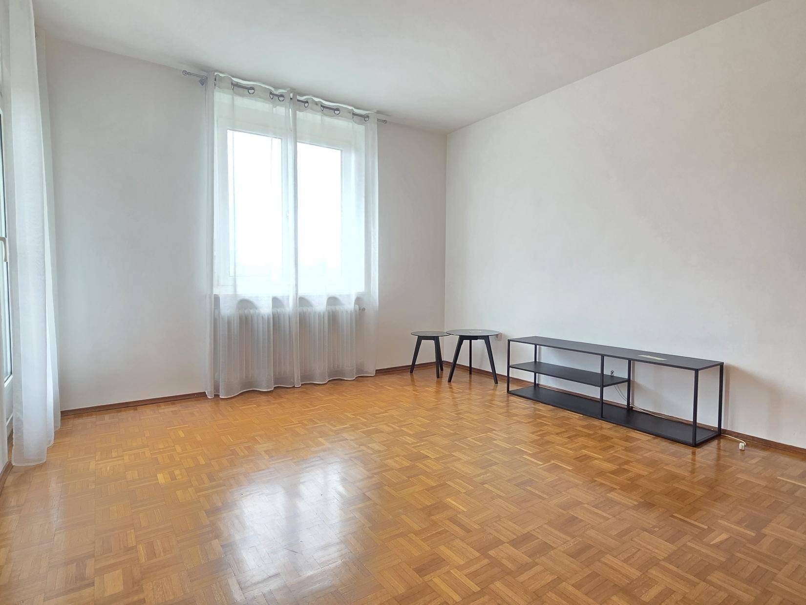 Heller Raum mit Parkettboden, großen Fenstern und minimalistischer Einrichtung.