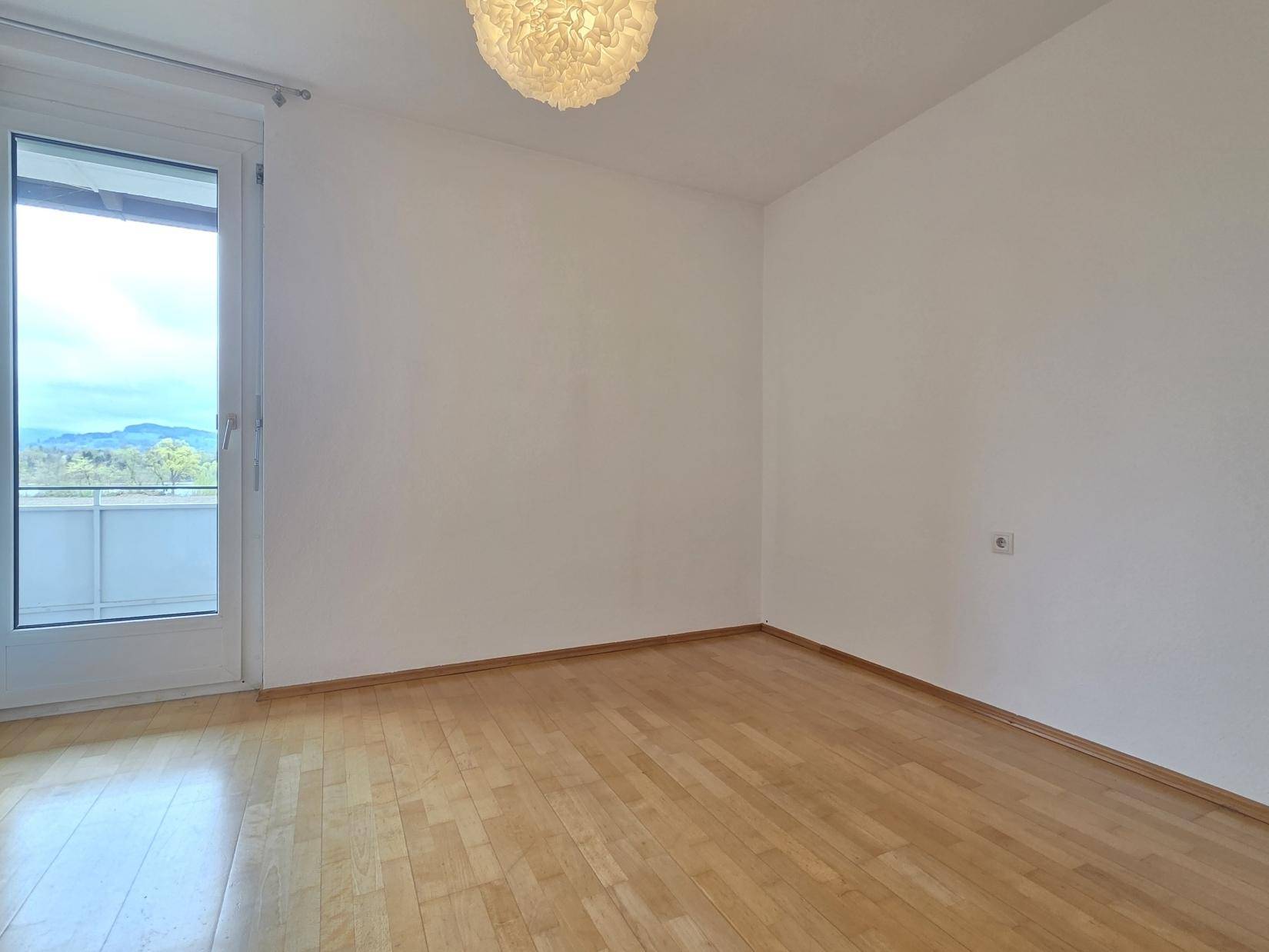 Geräumiges Zimmer mit hellem Holzboden und Zugang zu einem Balkon oder einer Terrasse.