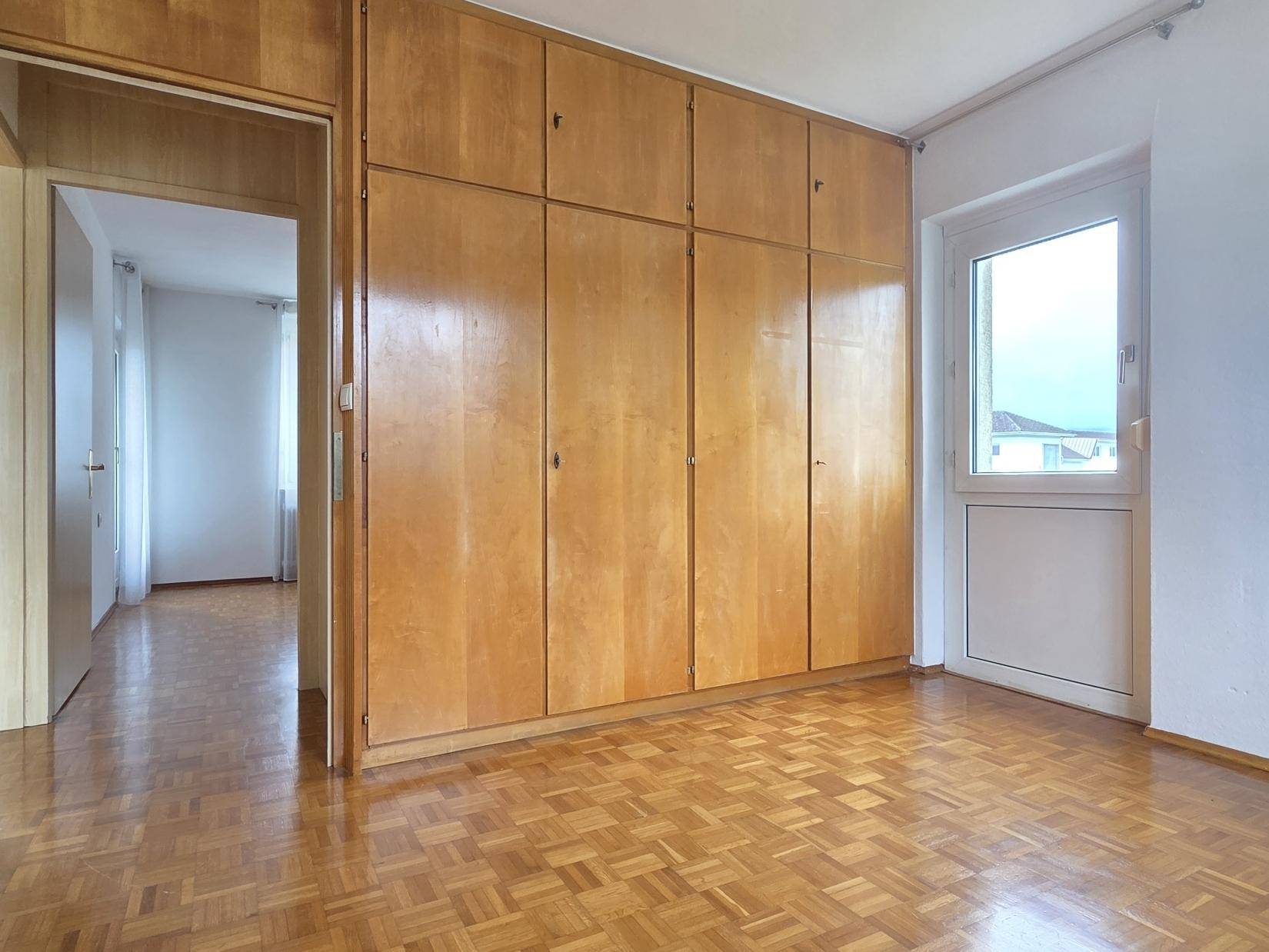 Schlafzimmer mit Einbauschränken, Parkettboden und Zugang zu einem Außenbereich.