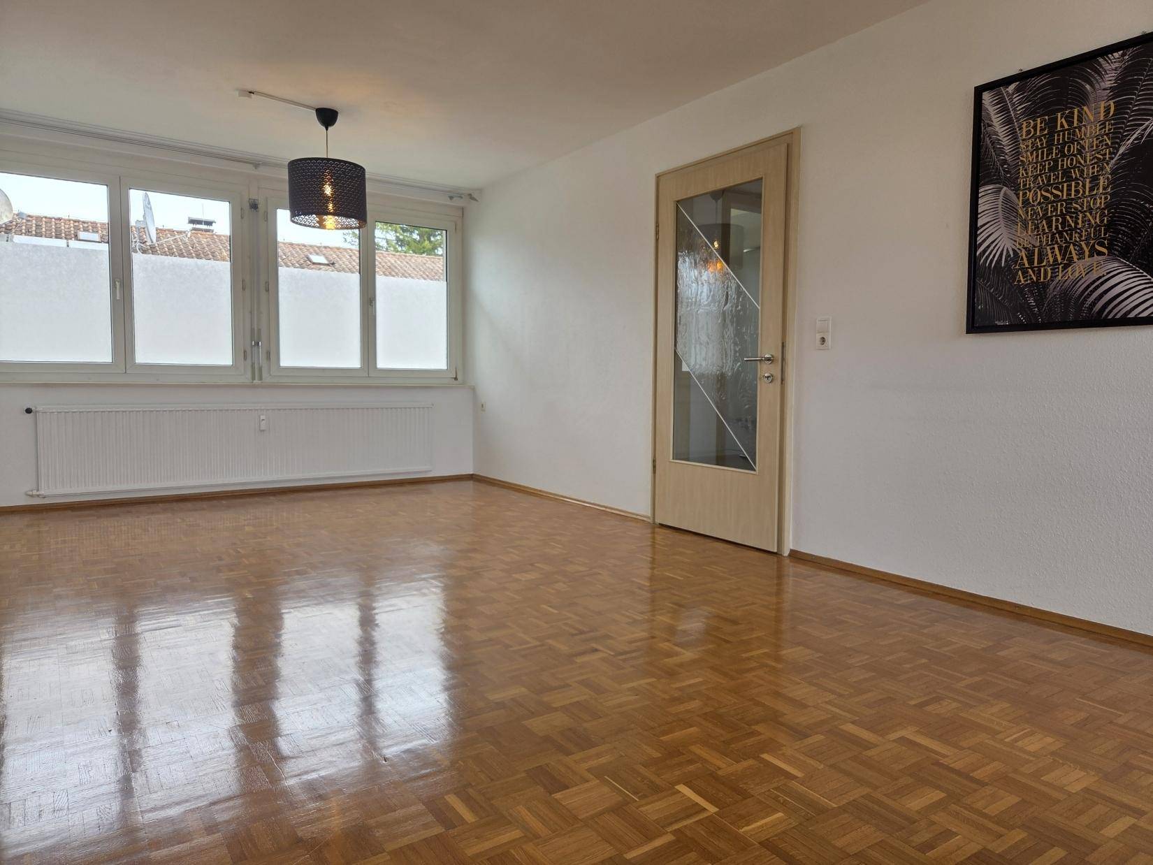 Helles Wohnzimmer mit Parkettboden, weißen Wänden und Blick nach draußen.