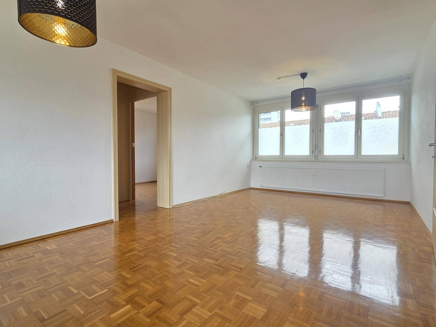 Heller Wohnbereich mit Parkettboden und Zugang zu weiteren Räumen, ideal für offenes Wohnen.