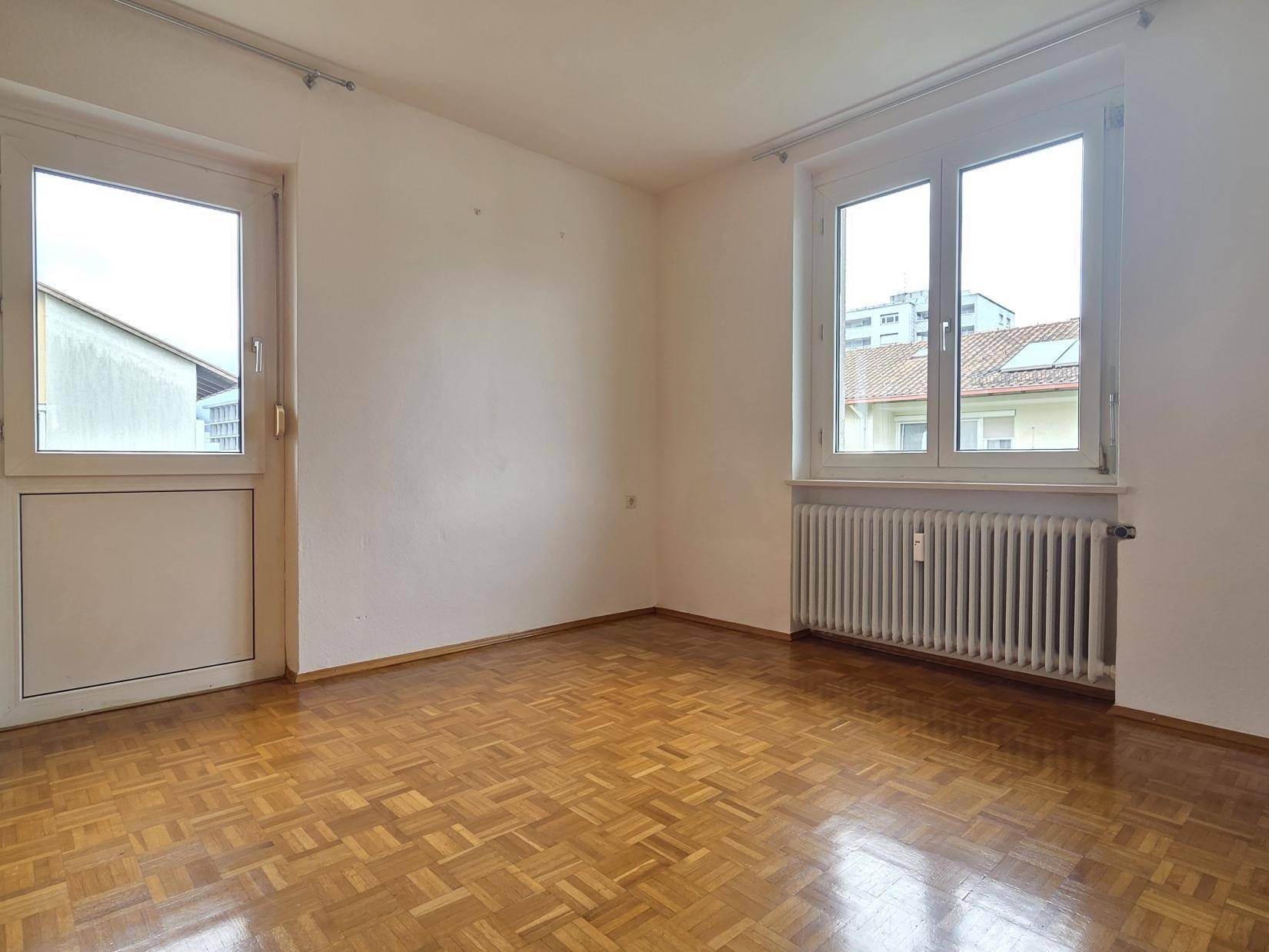 Helles Zimmer mit Parkettboden, Fenster und Tür zum Außenbereich, bietet viel Tageslicht.