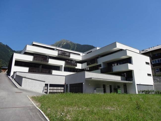 Modernes Apartmentgebäude mit gestufter Architektur und Balkonen vor einer Bergkulisse.