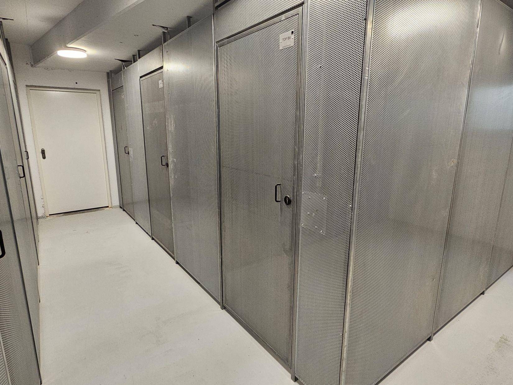 Reihe von abschließbaren Lagerabteilen aus Metall in einem Kellerraum.