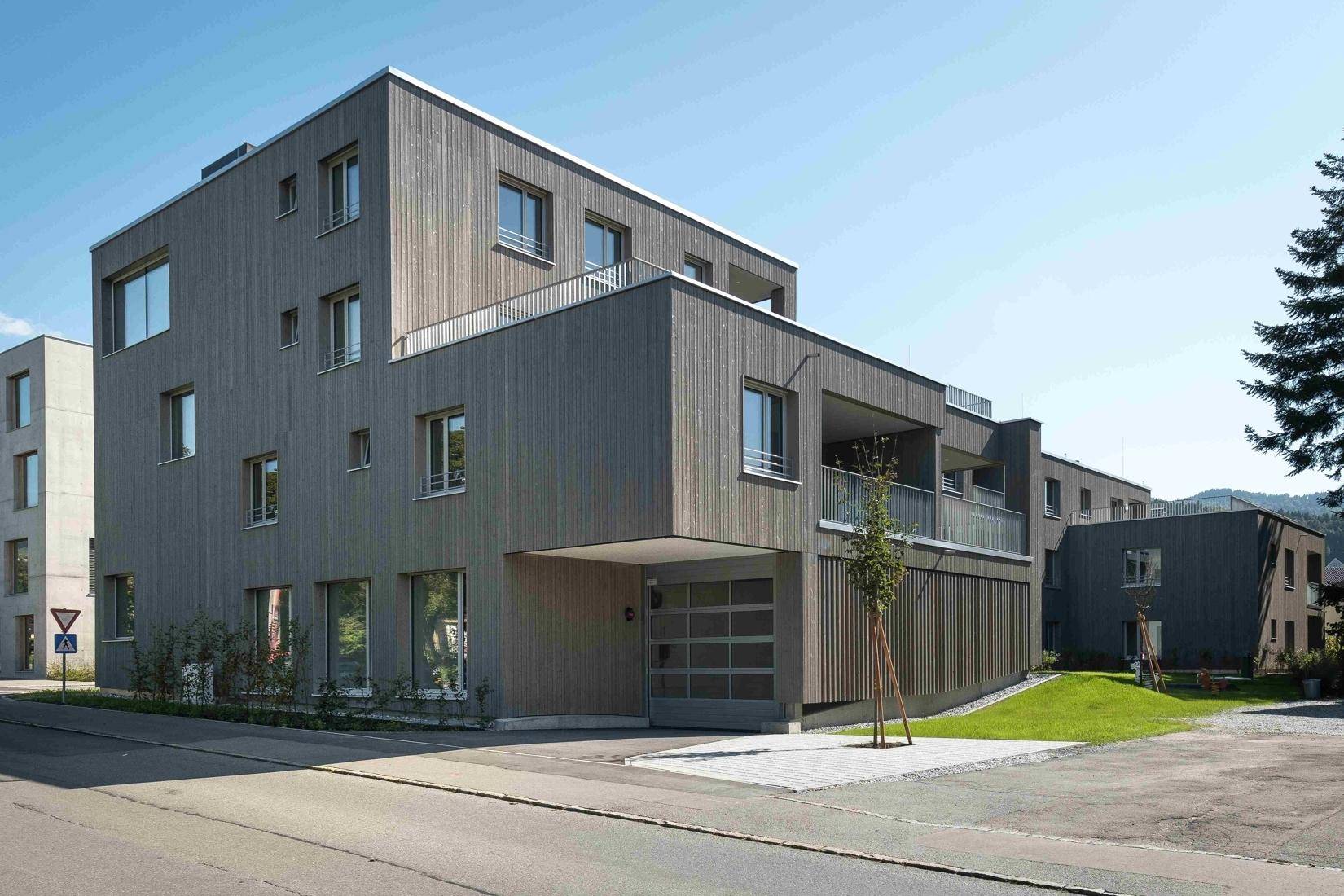 Außenansicht des modernen Gebäudes von der Straße mit Garagenzufahrt und Balkonen.