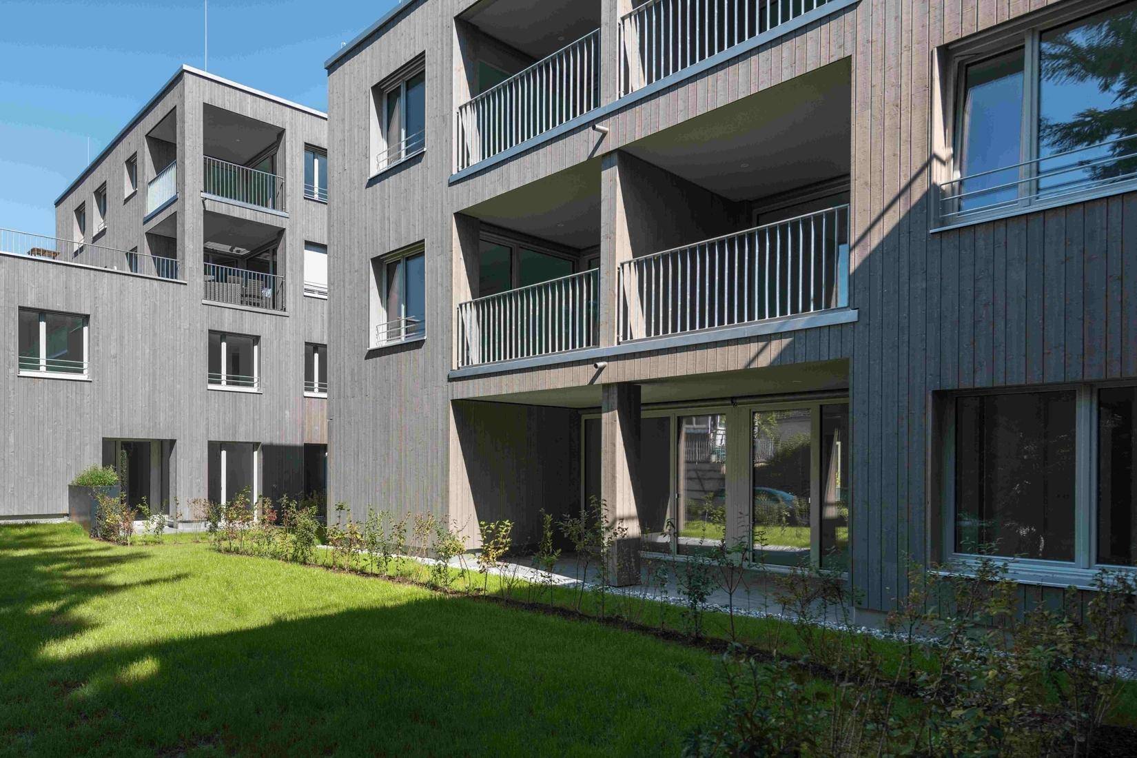Ansicht des modernen Gebäudes mit Balkonen und gepflegter Rasenfläche im Vordergrund.