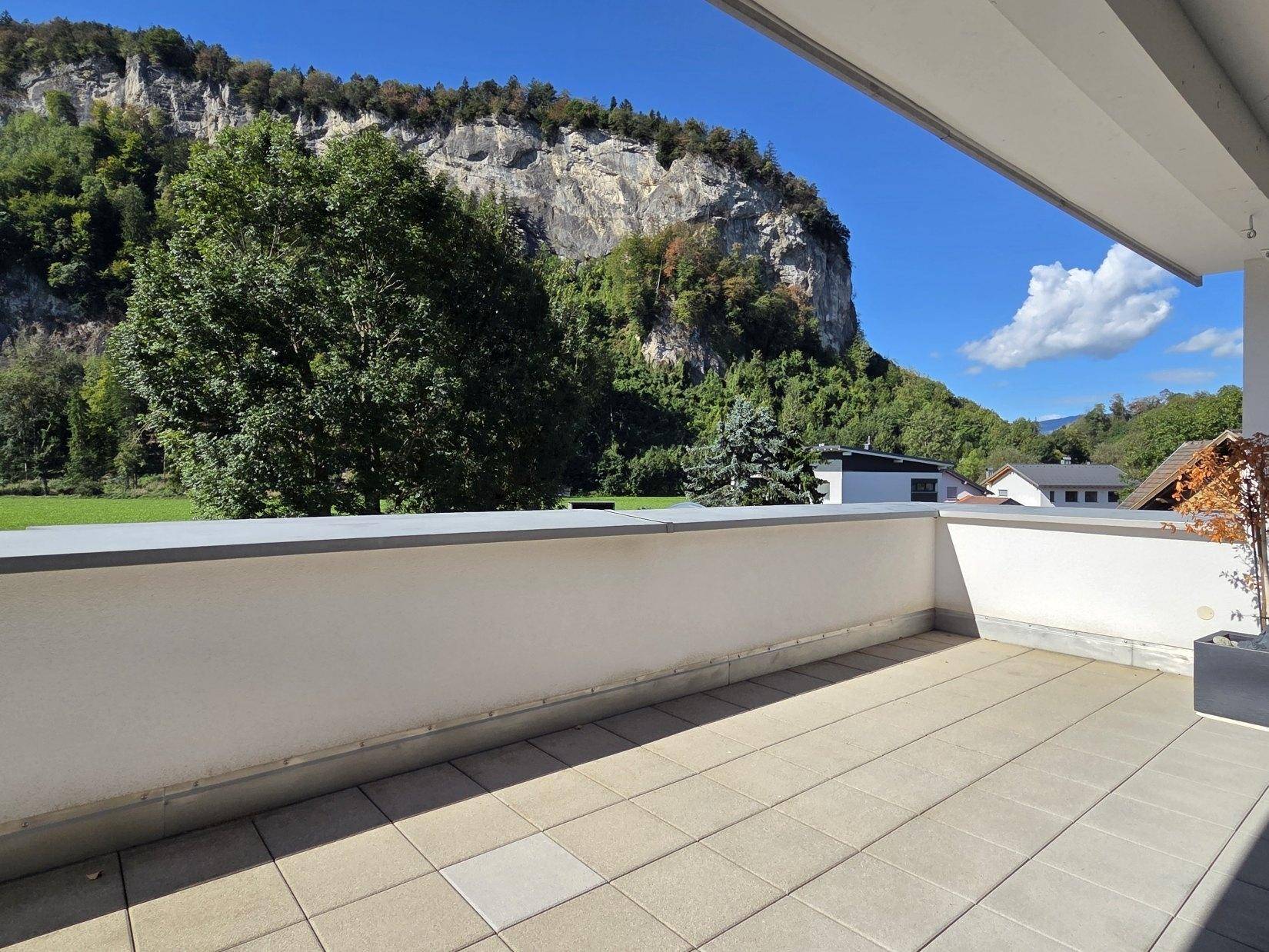 Großzügige Terrasse mit Fliesenboden und beeindruckendem Blick auf die majestätische Felswand und grüne Landschaft.
