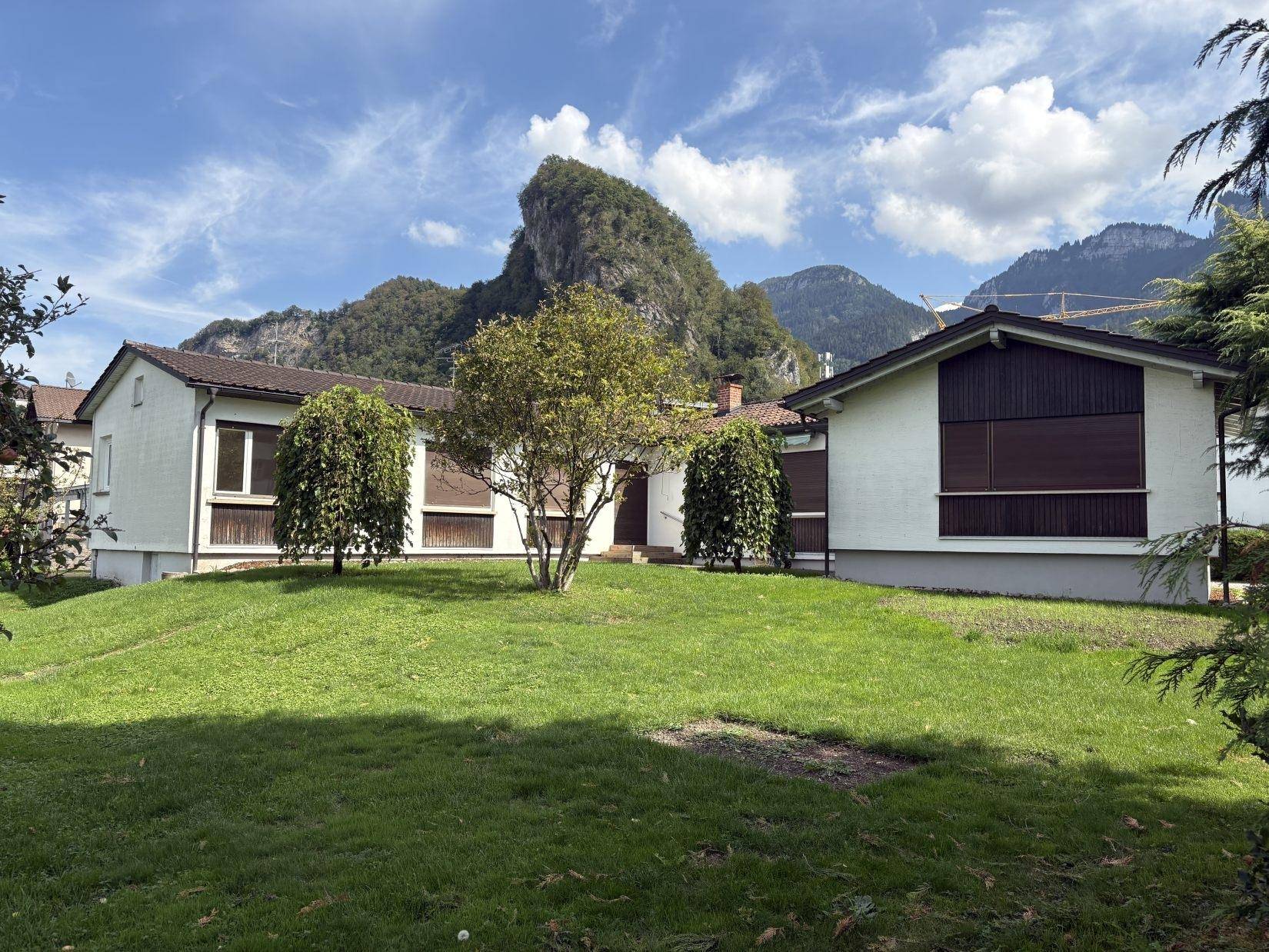 Ansicht des Hauses mit gepflegtem Rasen und Bergen im Hintergrund unter einem bewölkten Himmel.