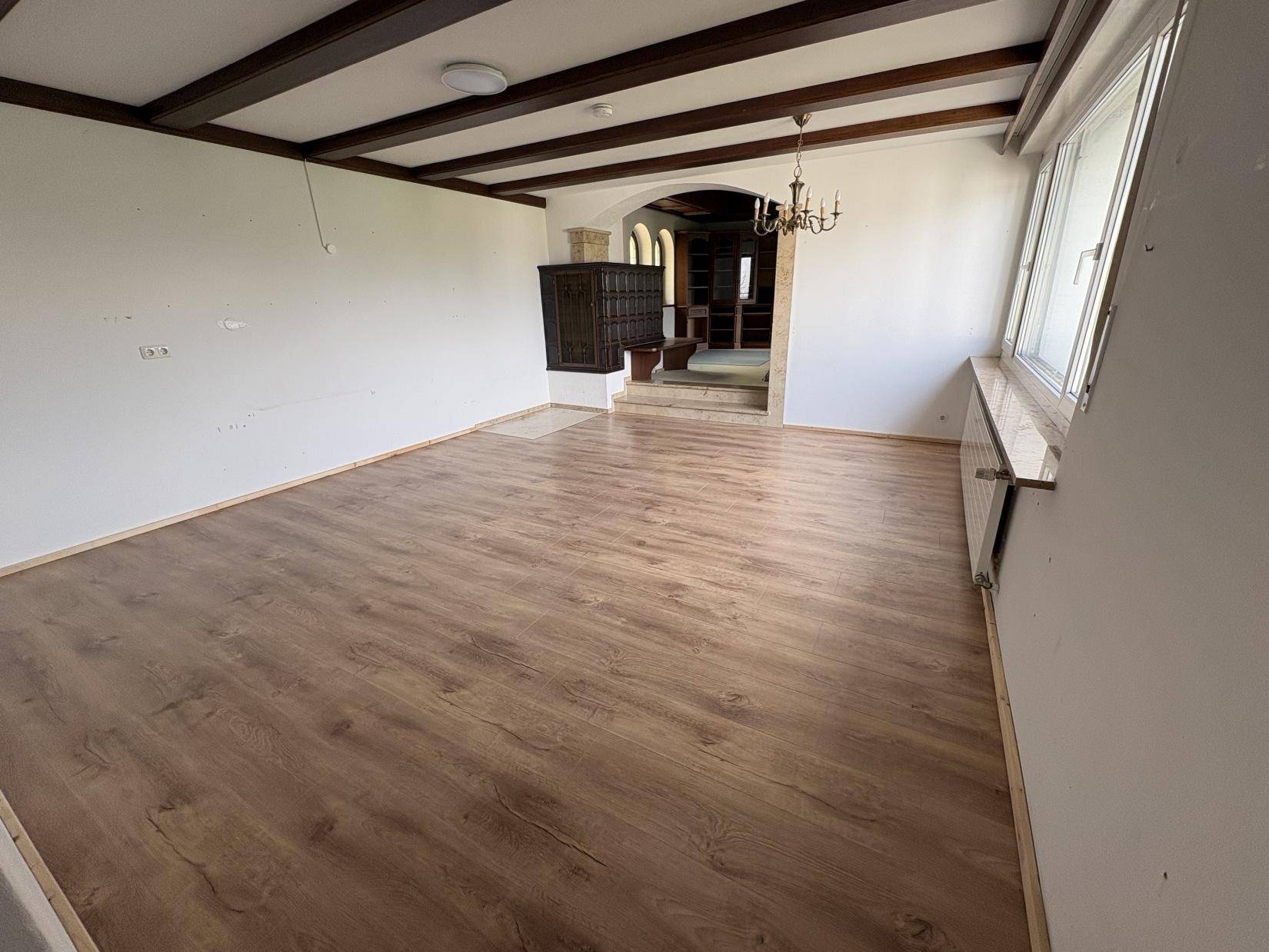 Helles Wohnzimmer mit neu verlegtem Laminatboden und sichtbaren Deckenbalken.