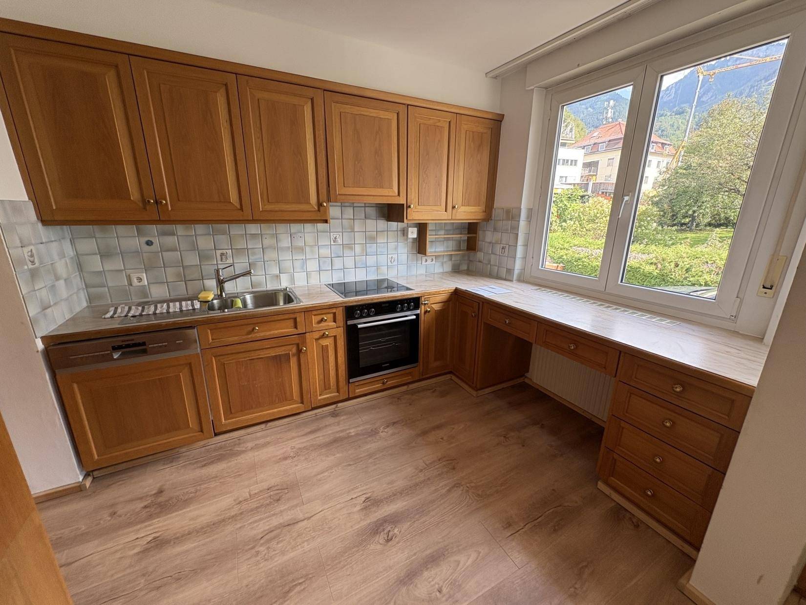 Funktionale Küche mit Holzschränken, Fliesenrückwand und Fenster mit Bergblick.