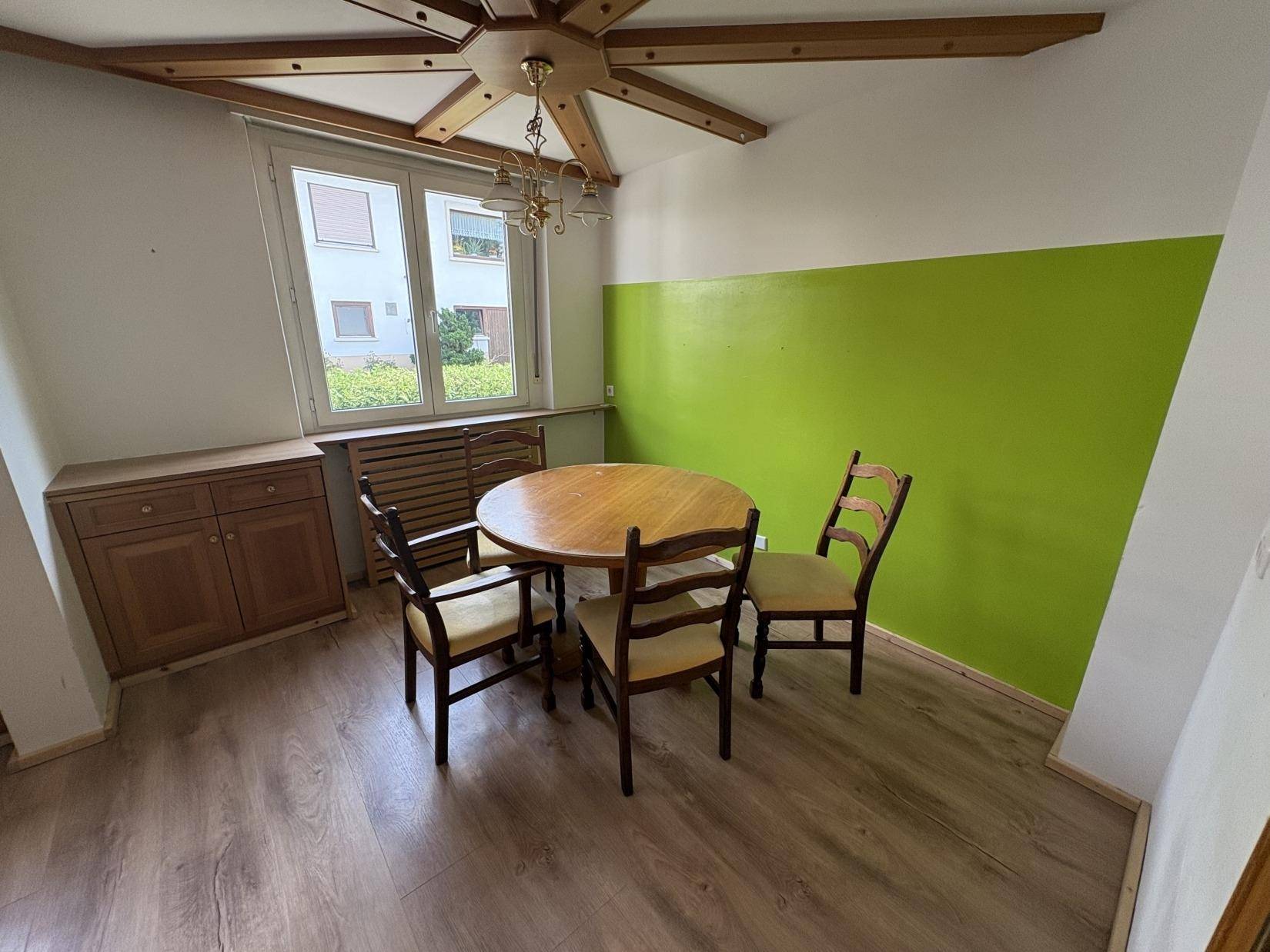 Gemütlicher Essbereich mit Holztisch, Stühlen und grüner Akzentwand.