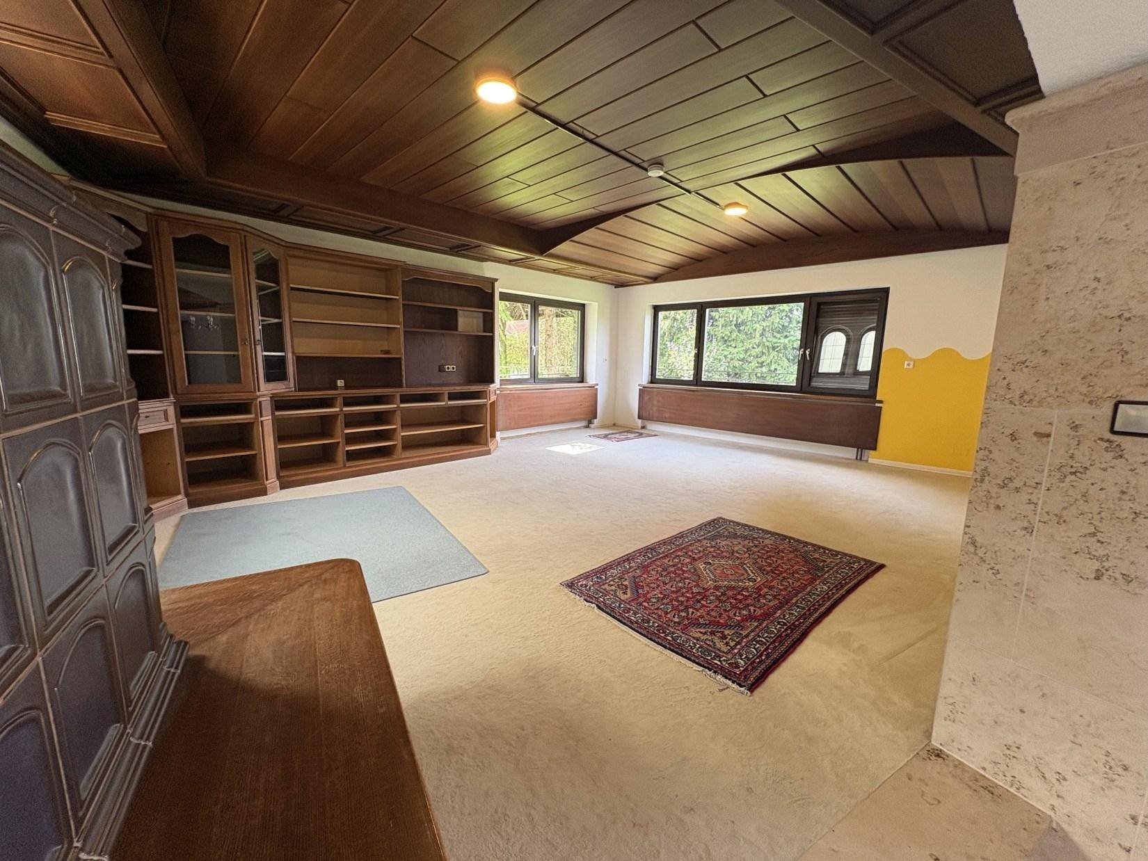 Großes Wohnzimmer mit Holzkassettendecke, Einbauschränken und Blick ins Grüne.